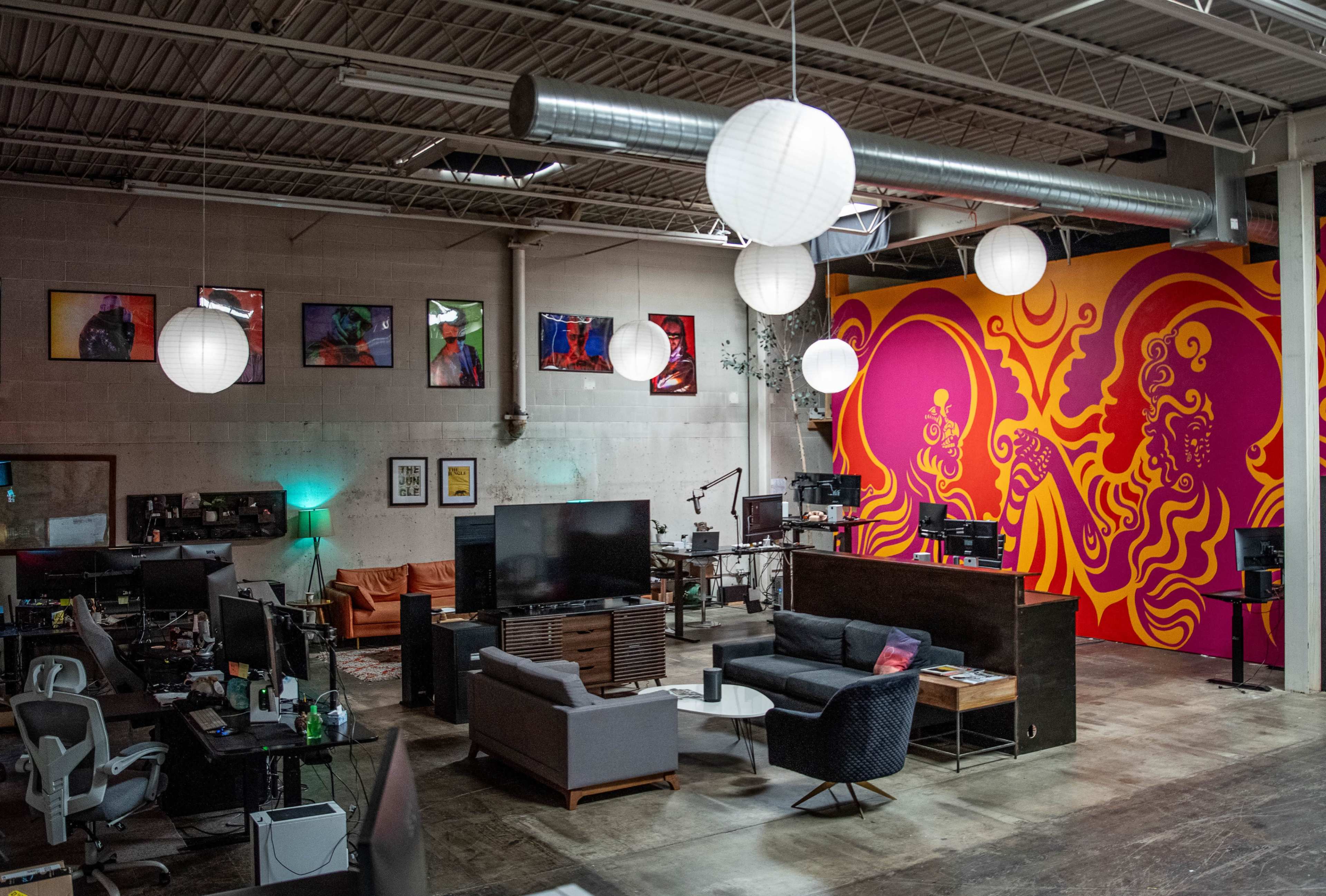 A spacious office or creative workspace with colorful wall art, various seating arrangements, and multiple workstations equipped with computers.