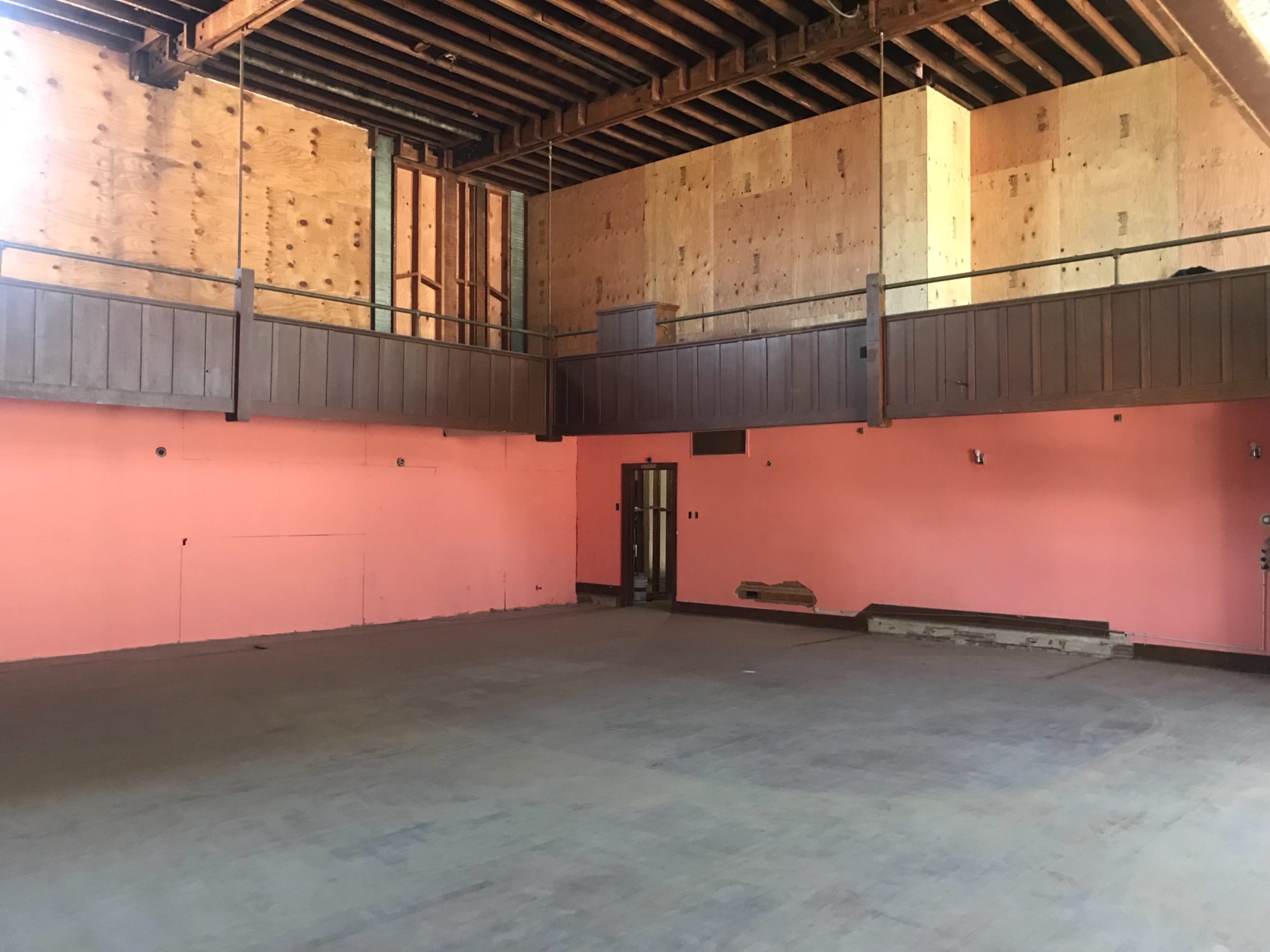 An empty room with pink walls, wooden beams, and a section of elevated flooring along the back wall.