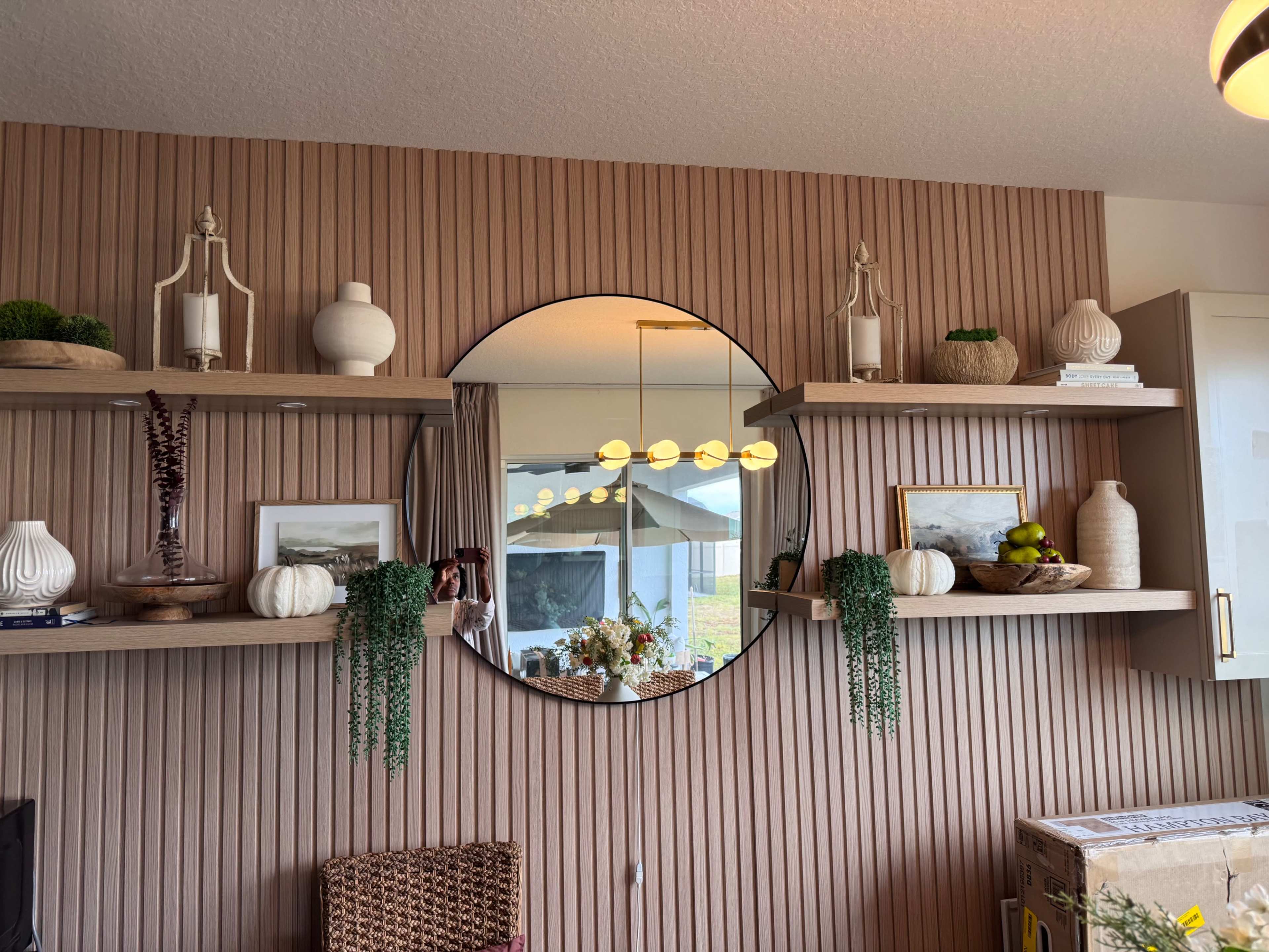 The image shows a living room wall adorned with round mirrors and two floating shelves displaying decorative items, including vases, plants, and framed pictures.