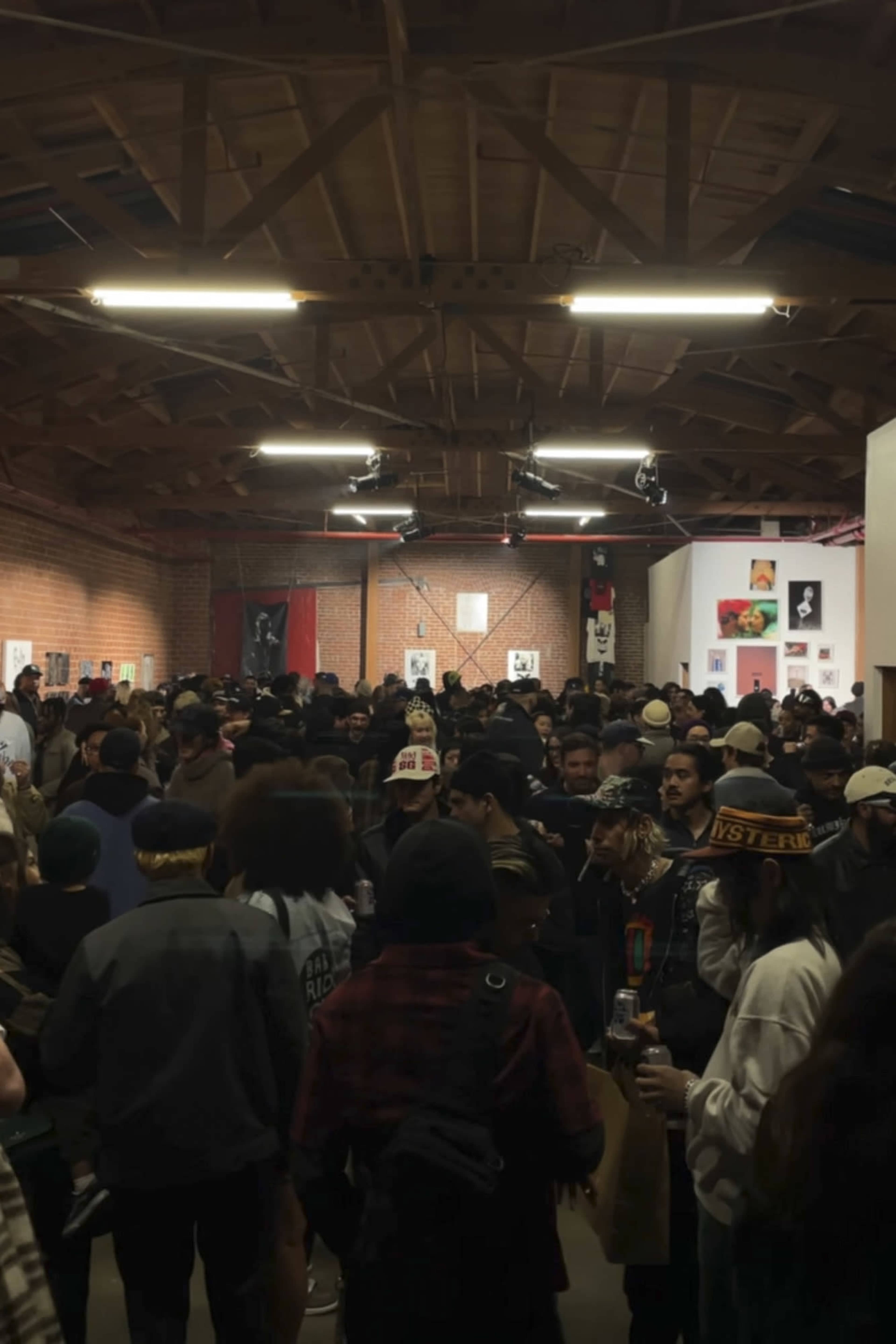 A large crowd gathers in an art gallery filled with various artworks on the walls.