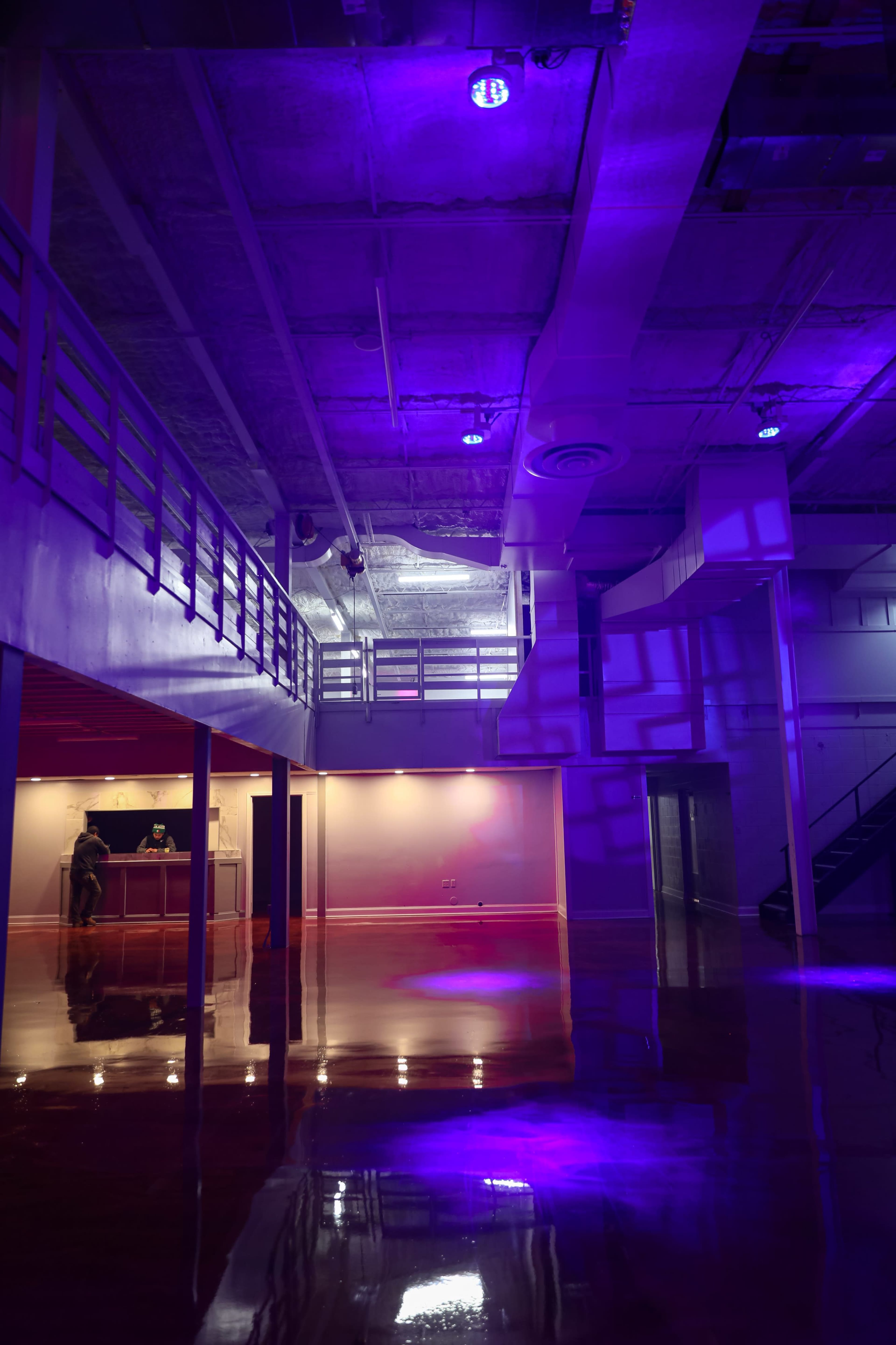 The image shows a spacious, modern interior with purple lighting, featuring a polished floor and an upper level visible through a railing.
