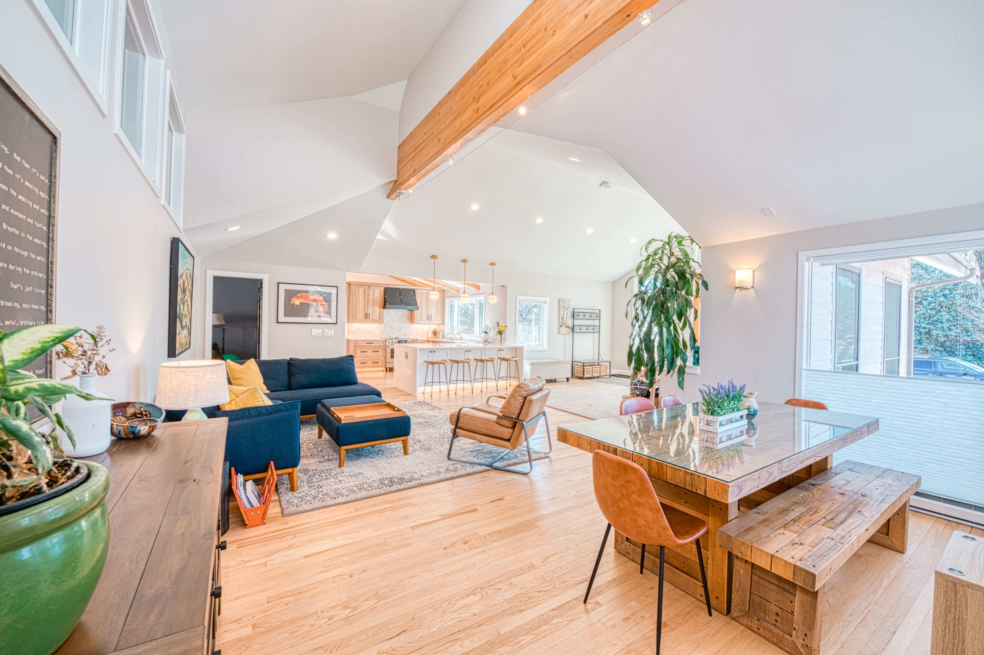 A modern living space features a blue sofa, a wooden dining table, and large windows that allow natural light to fill the room.