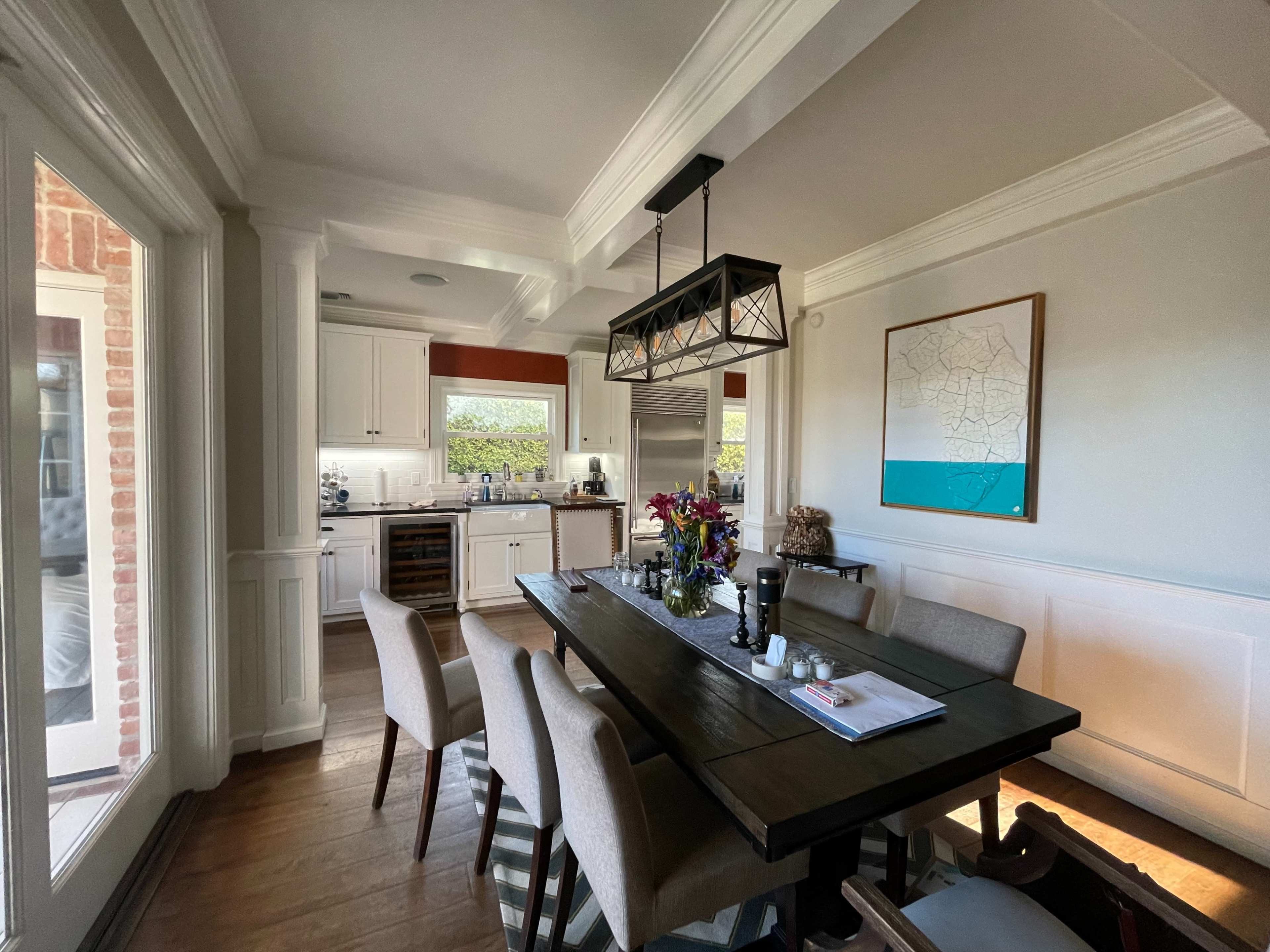 A modern dining area features a wooden table with chairs, surrounded by a spacious kitchen with stainless steel appliances and large windows.