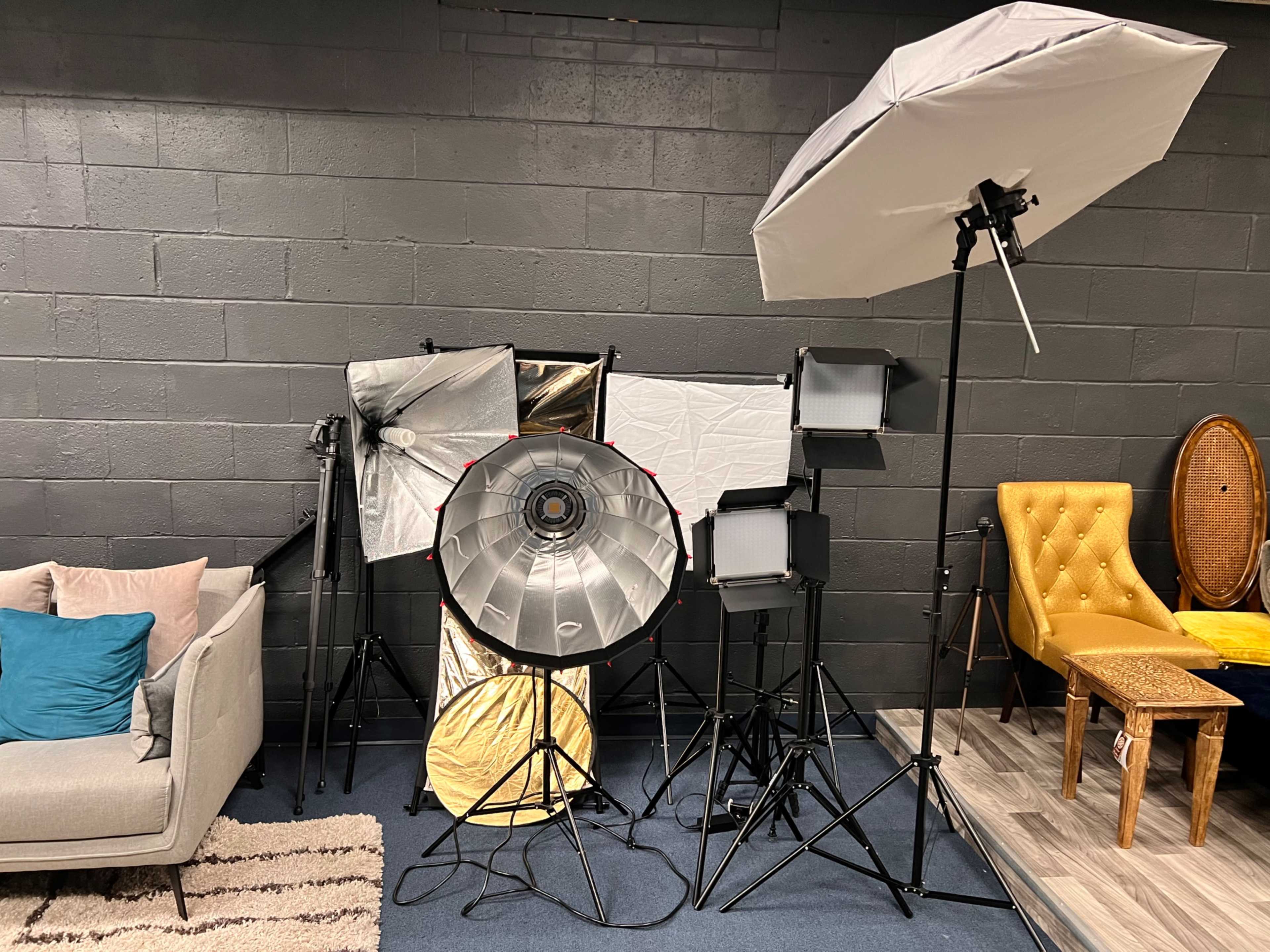 A photography setup featuring various softbox lights and reflectors arranged next to a beige sofa and a yellow chair in a studio space.