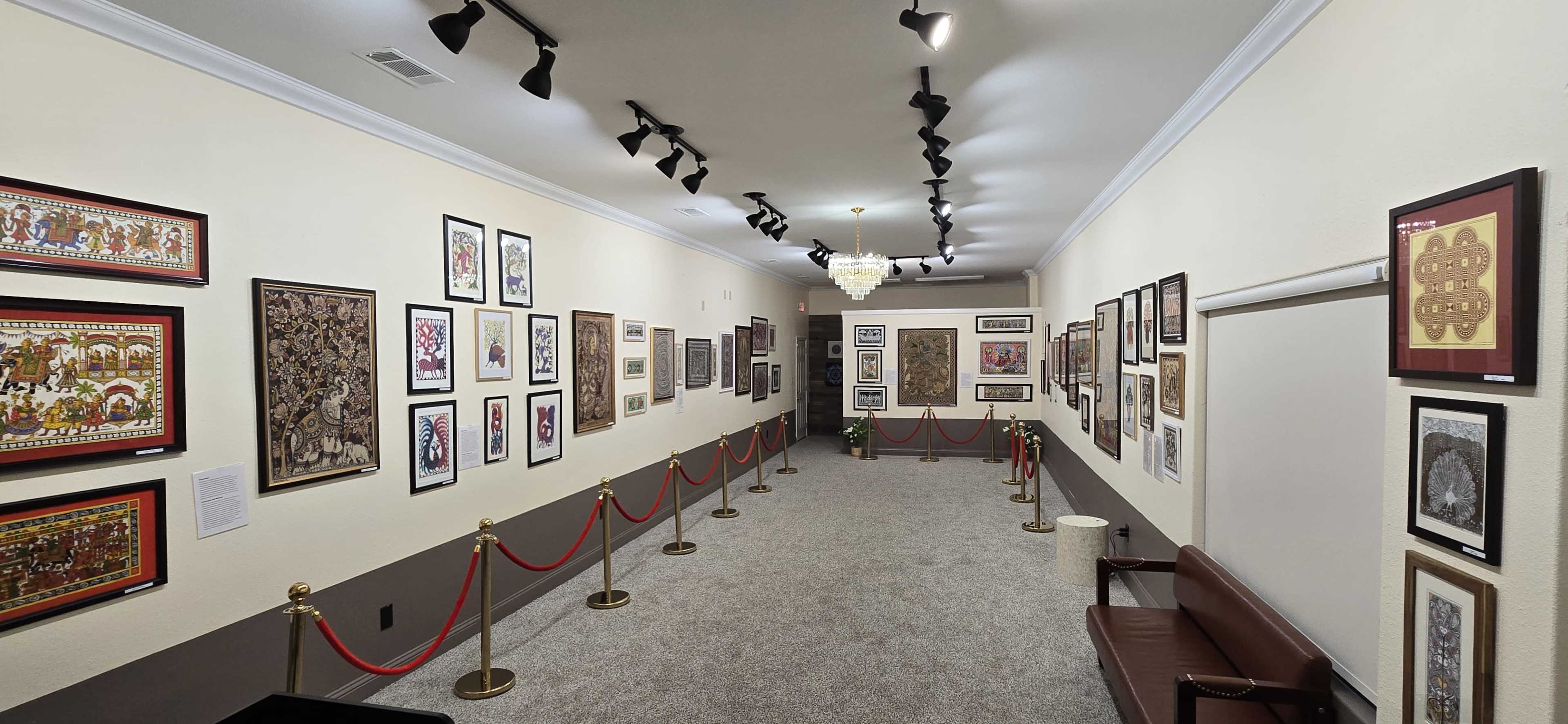 The image shows an art gallery corridor lined with framed artwork on the walls, with red ropes creating a barrier along the carpeted floor.