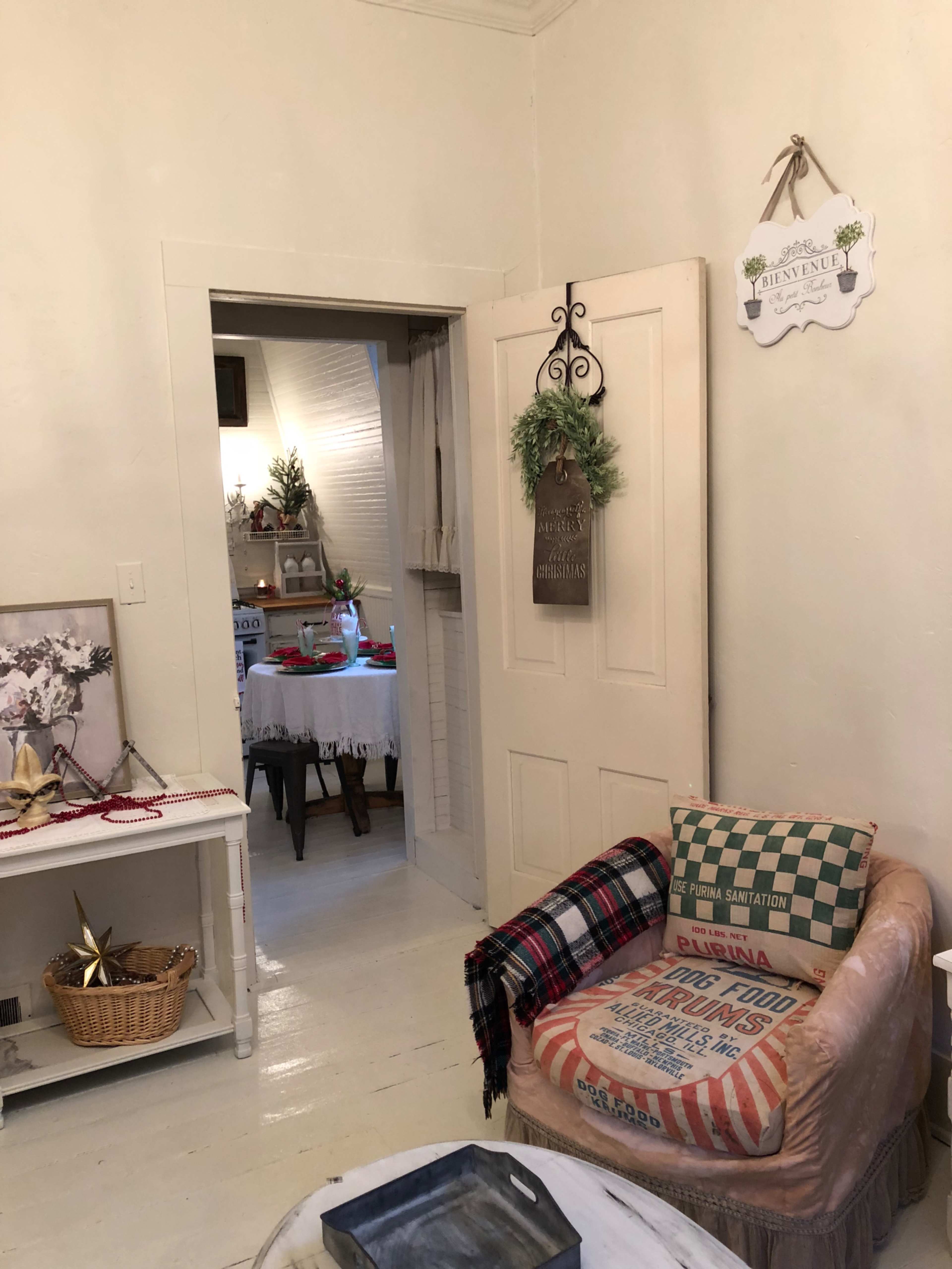 A cozy room features a vintage chair, a small table with decorations, and a doorway leading to another area.