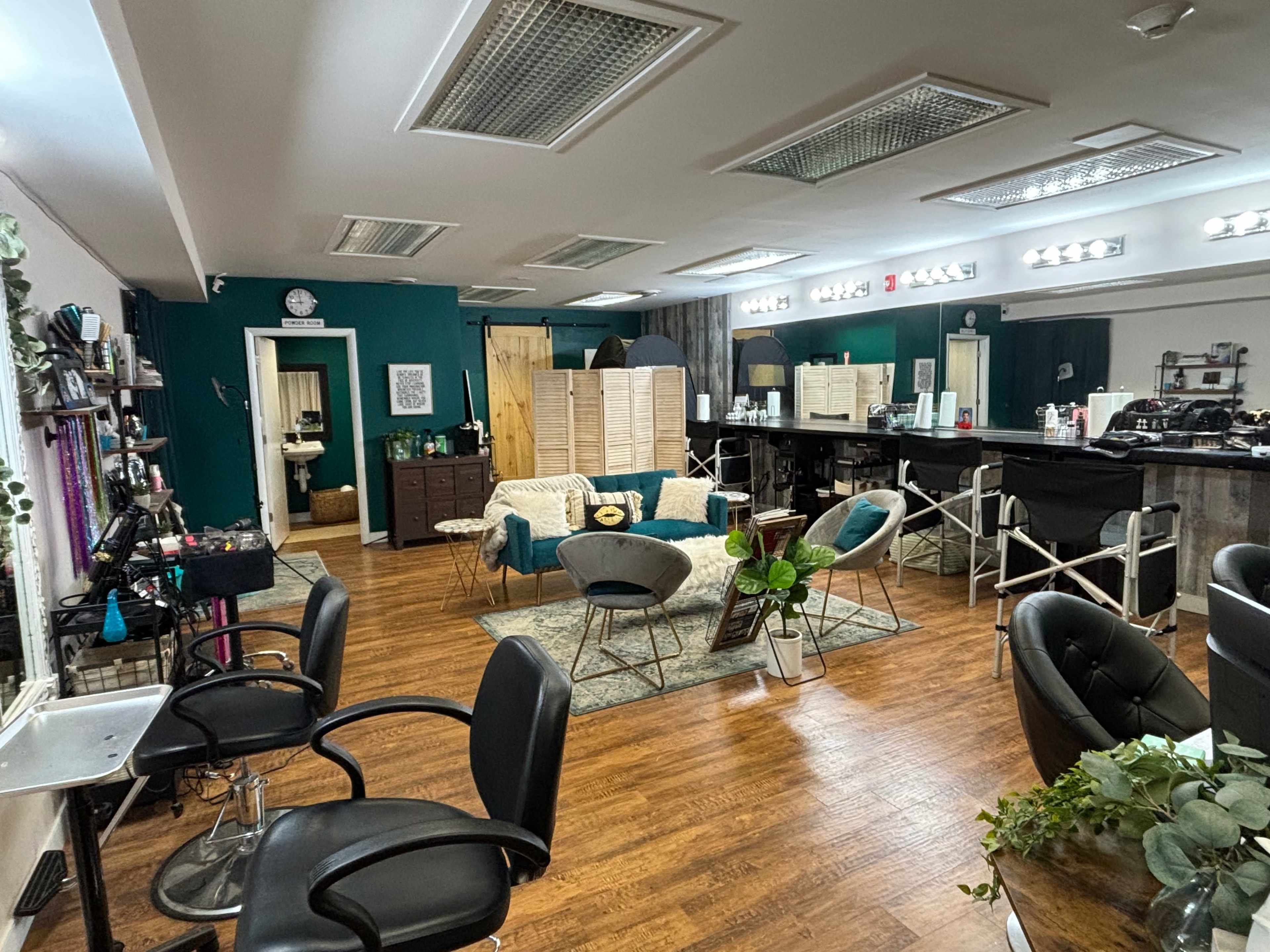 A spacious hair salon with chairs, mirrors, and various styling stations arranged around a central seating area.