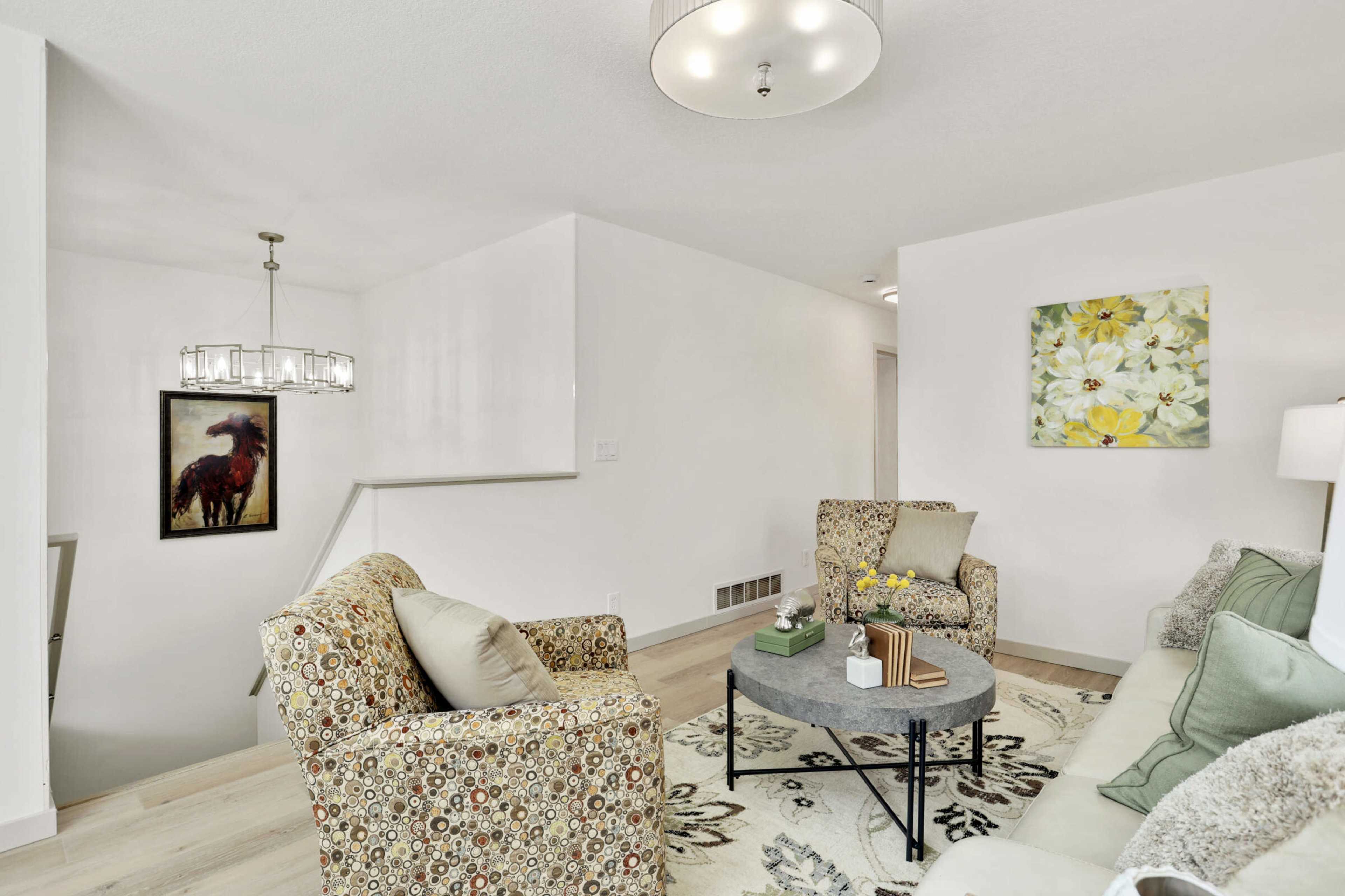A modern living room with two patterned chairs, a round coffee table, and a large floral painting on the wall.