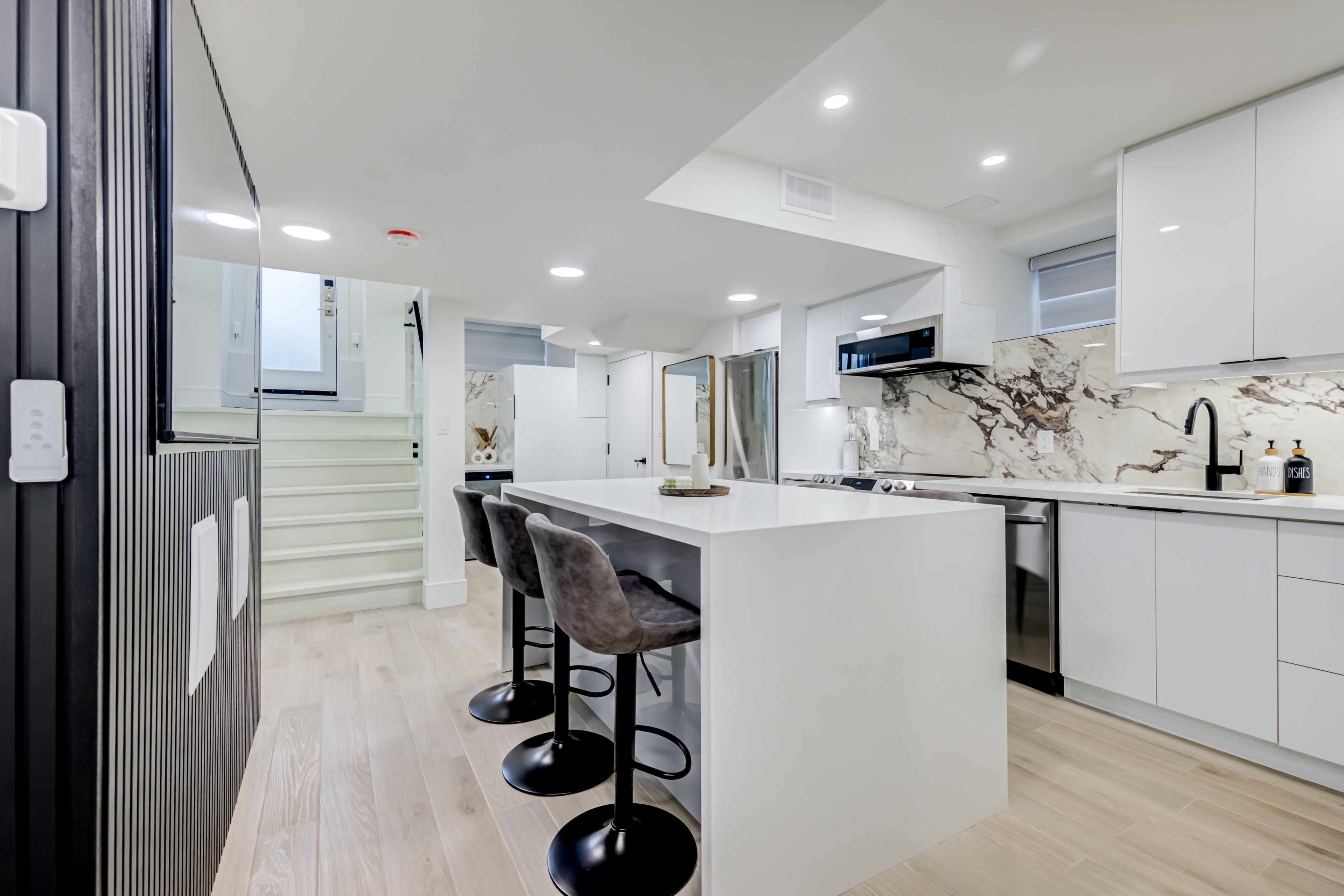 A modern kitchen with a white island, black bar stools, and marble accents on the walls and countertops.