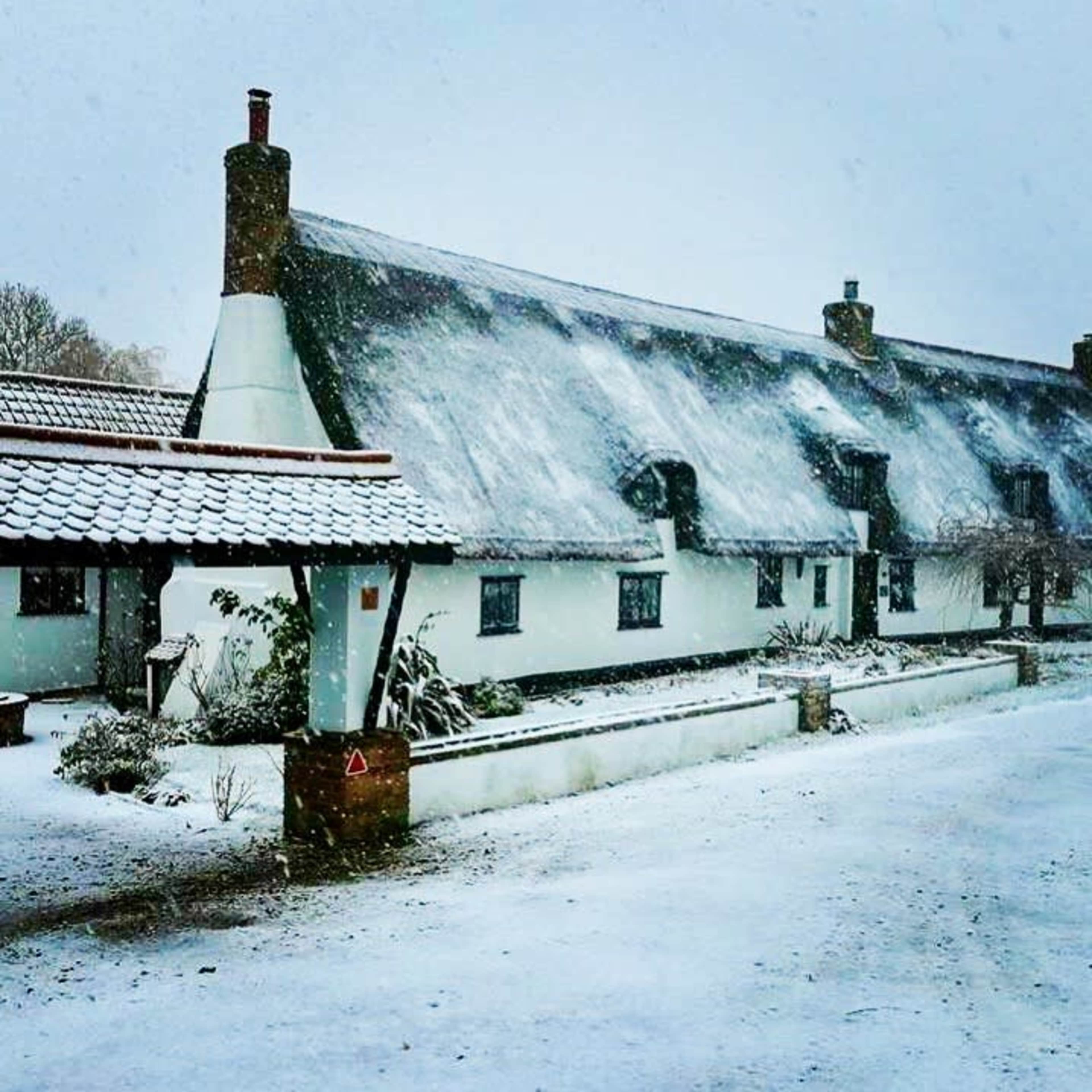 A snow-covered thatched-roof cottage is set against a cold winter landscape.