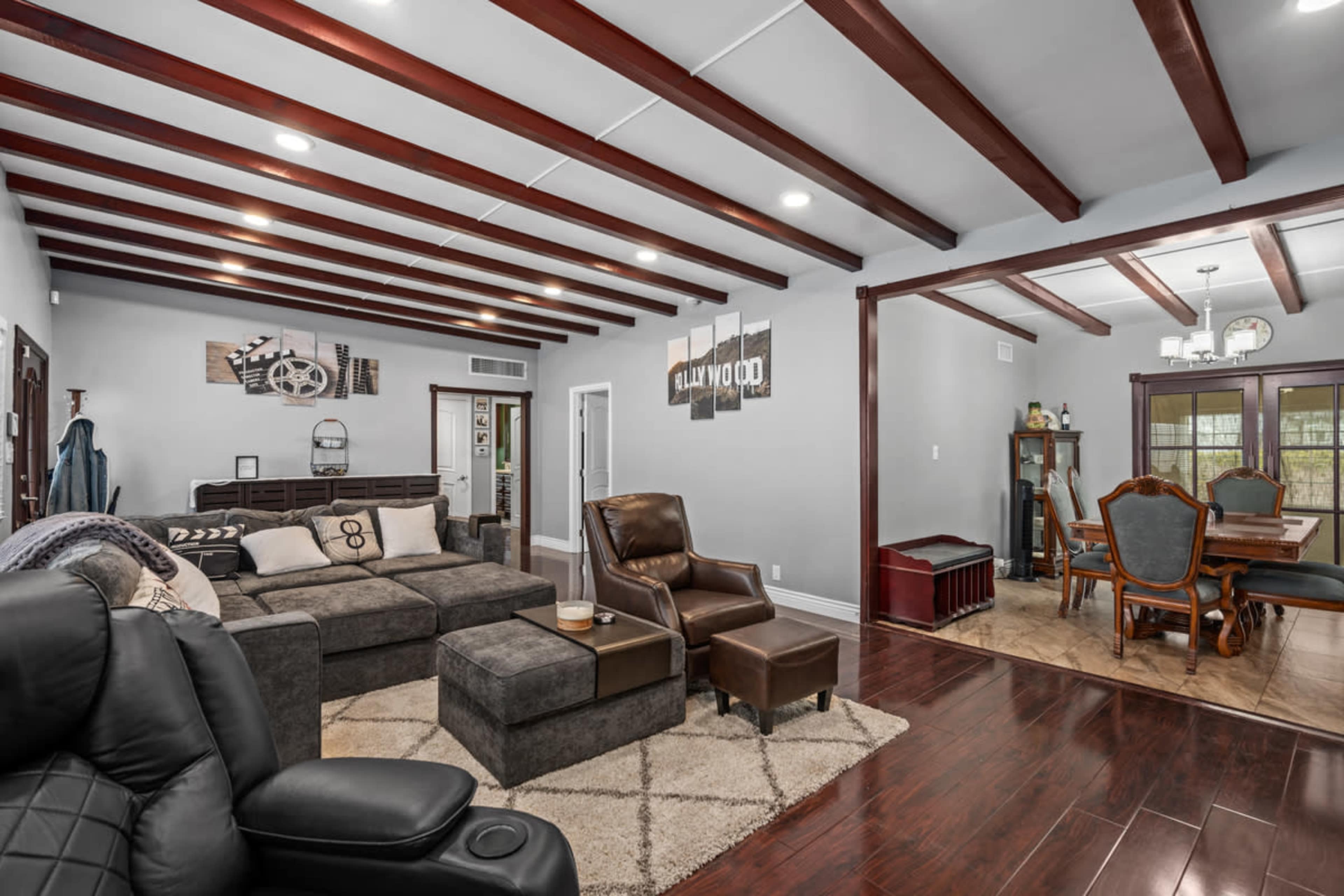 A spacious living room with a sectional sofa, a recliner, and wood beam ceilings, connected to a dining area featuring a table with chairs.
