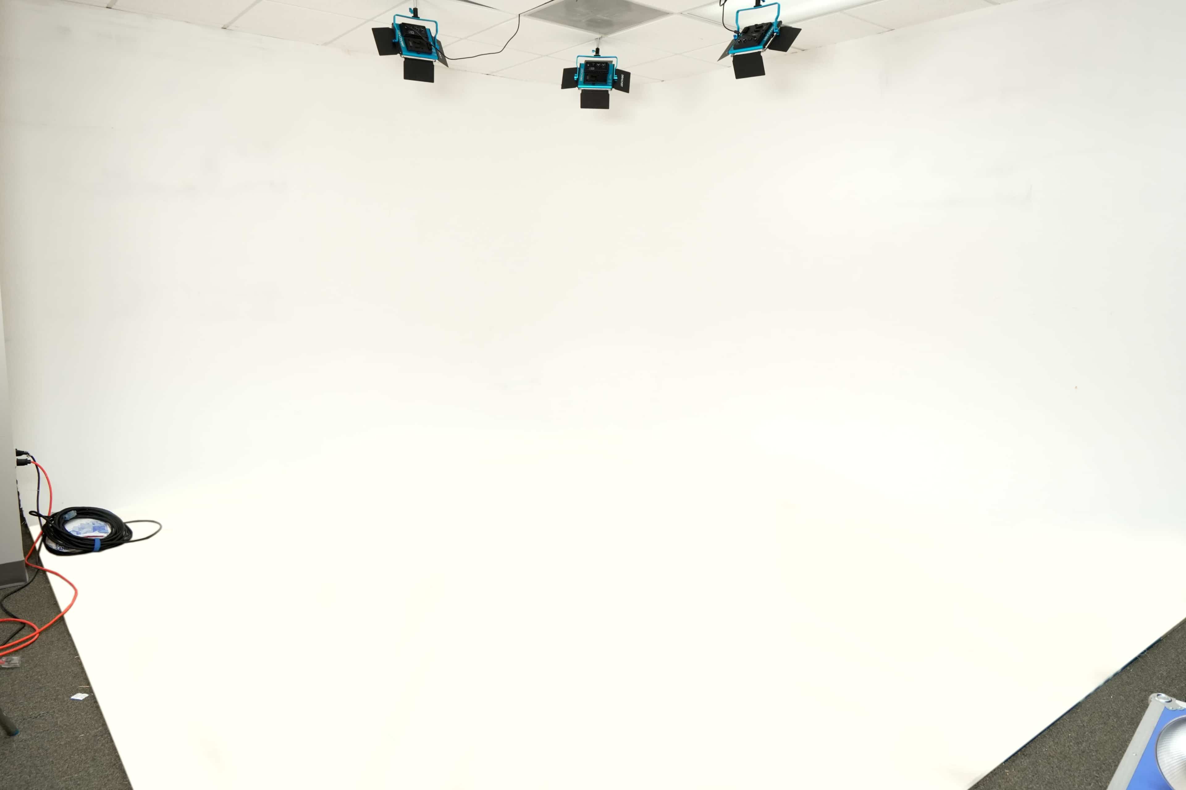 The image shows an empty white studio space with multiple overhead lights and a clean, uniform floor.