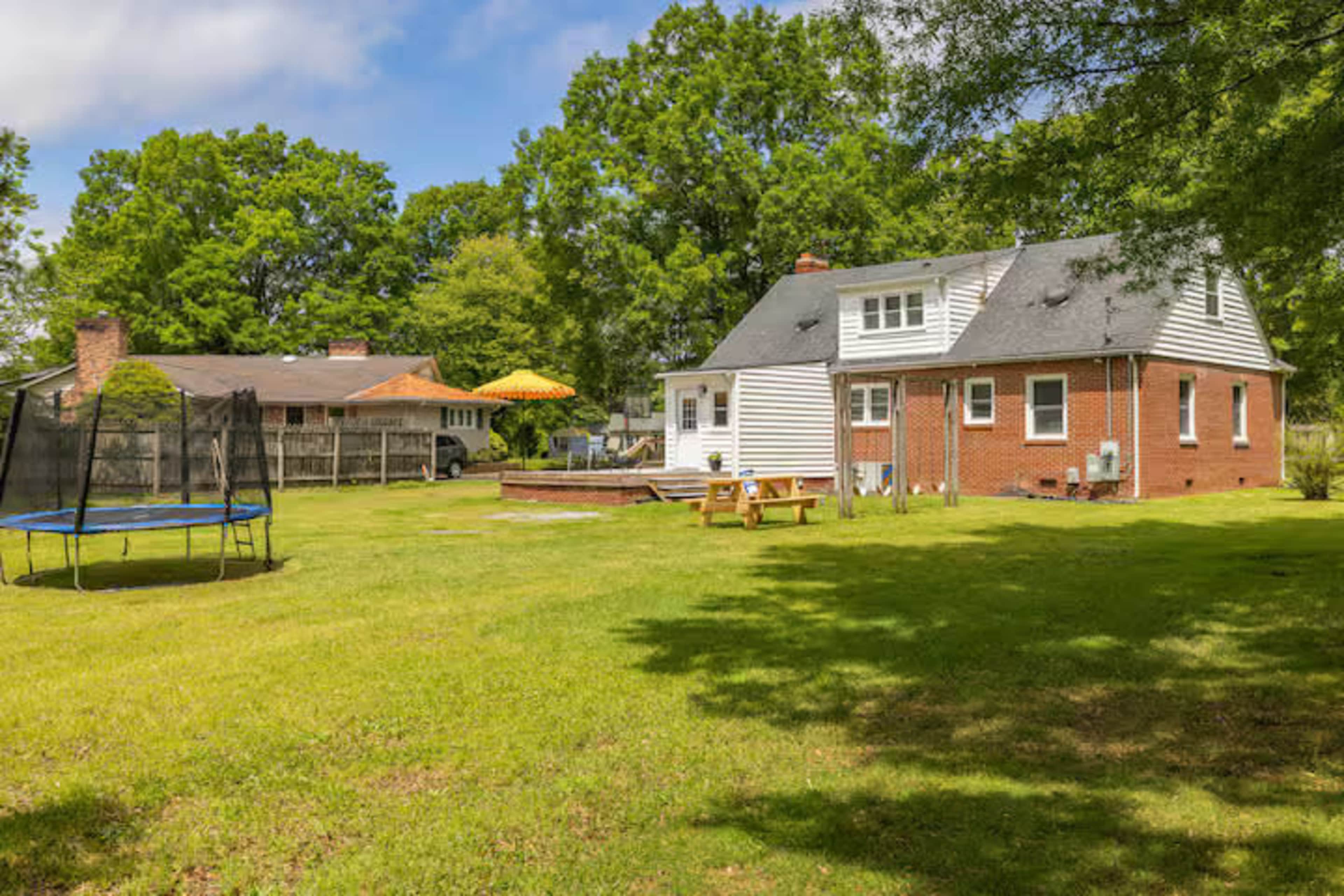 The image shows a backyard with a house, a trampoline, a picnic table, and a swimming pool area surrounded by trees.