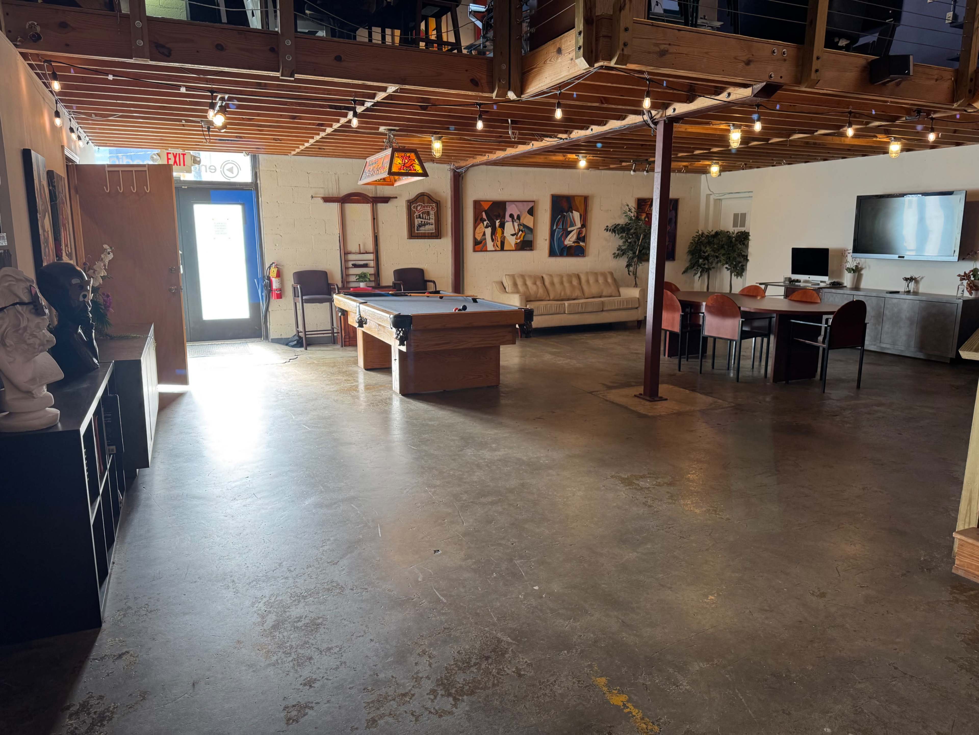 The image shows an open recreational space featuring a pool table, a sofa, dining area, and decorative artwork on the walls.