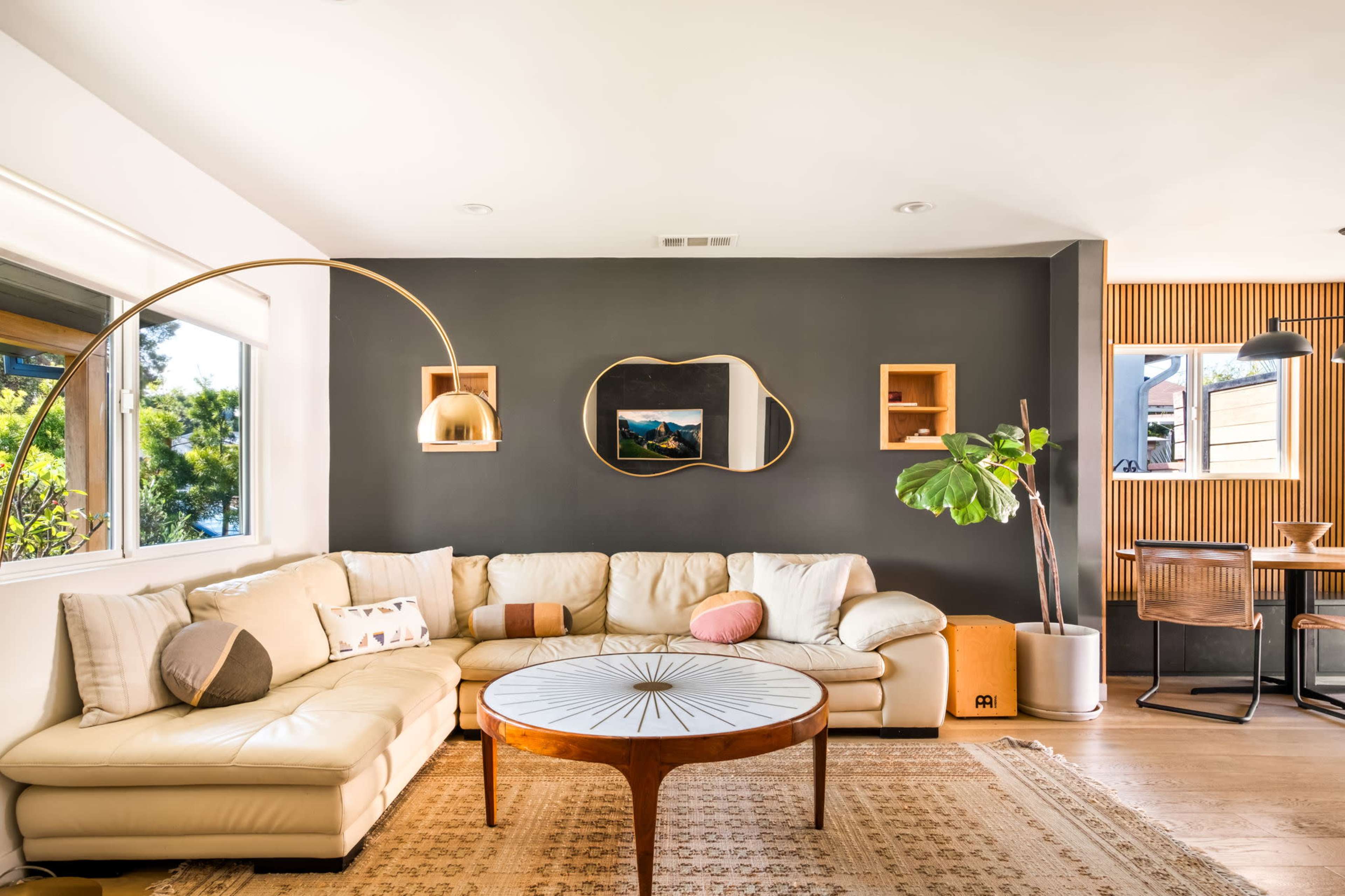 The living room features a large, curved sectional sofa, a round coffee table, and a wall adorned with a large mirror and framed artwork.