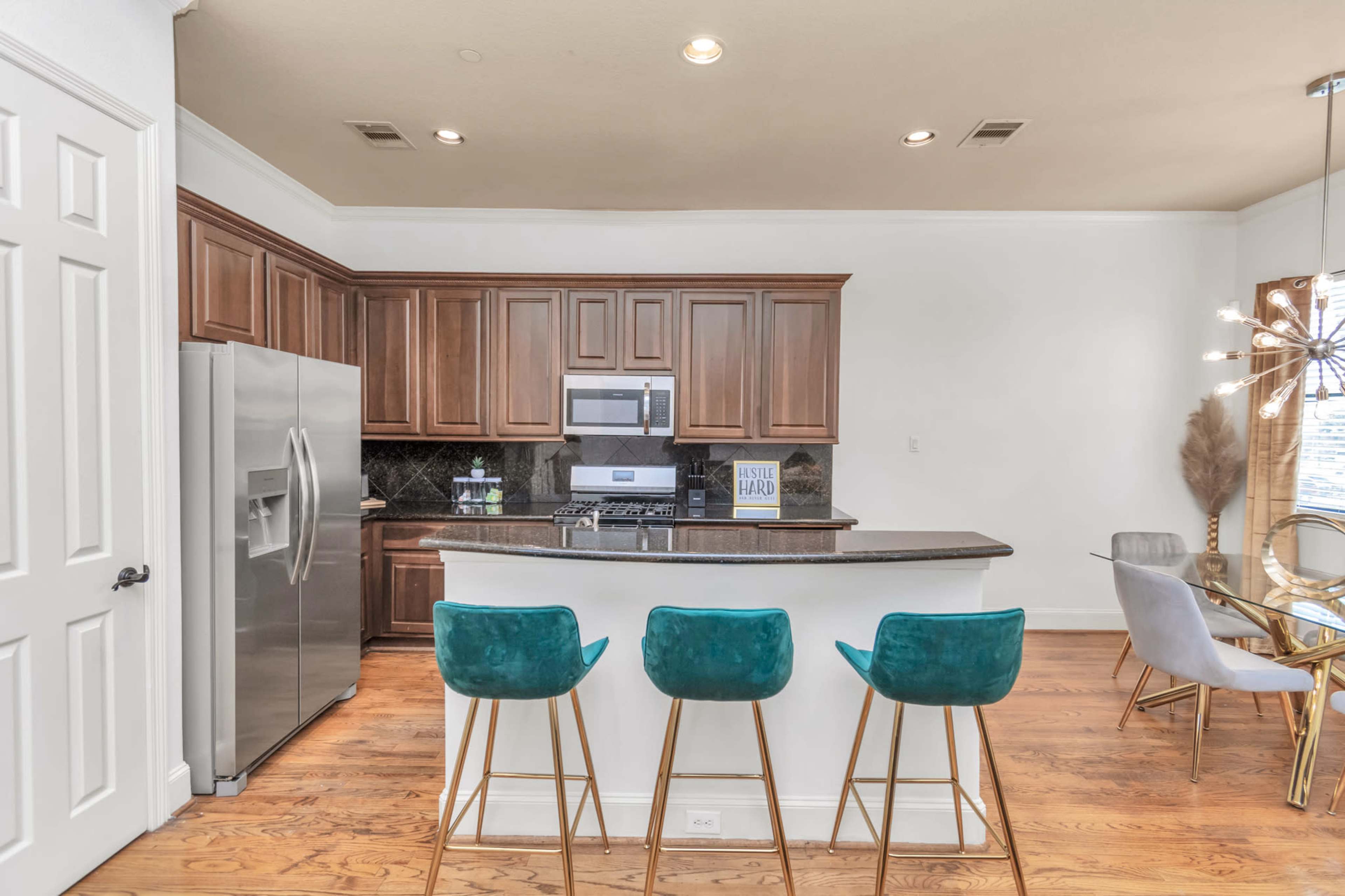 A modern kitchen with dark wood cabinetry, stainless steel appliances, and a breakfast bar with three teal stools.