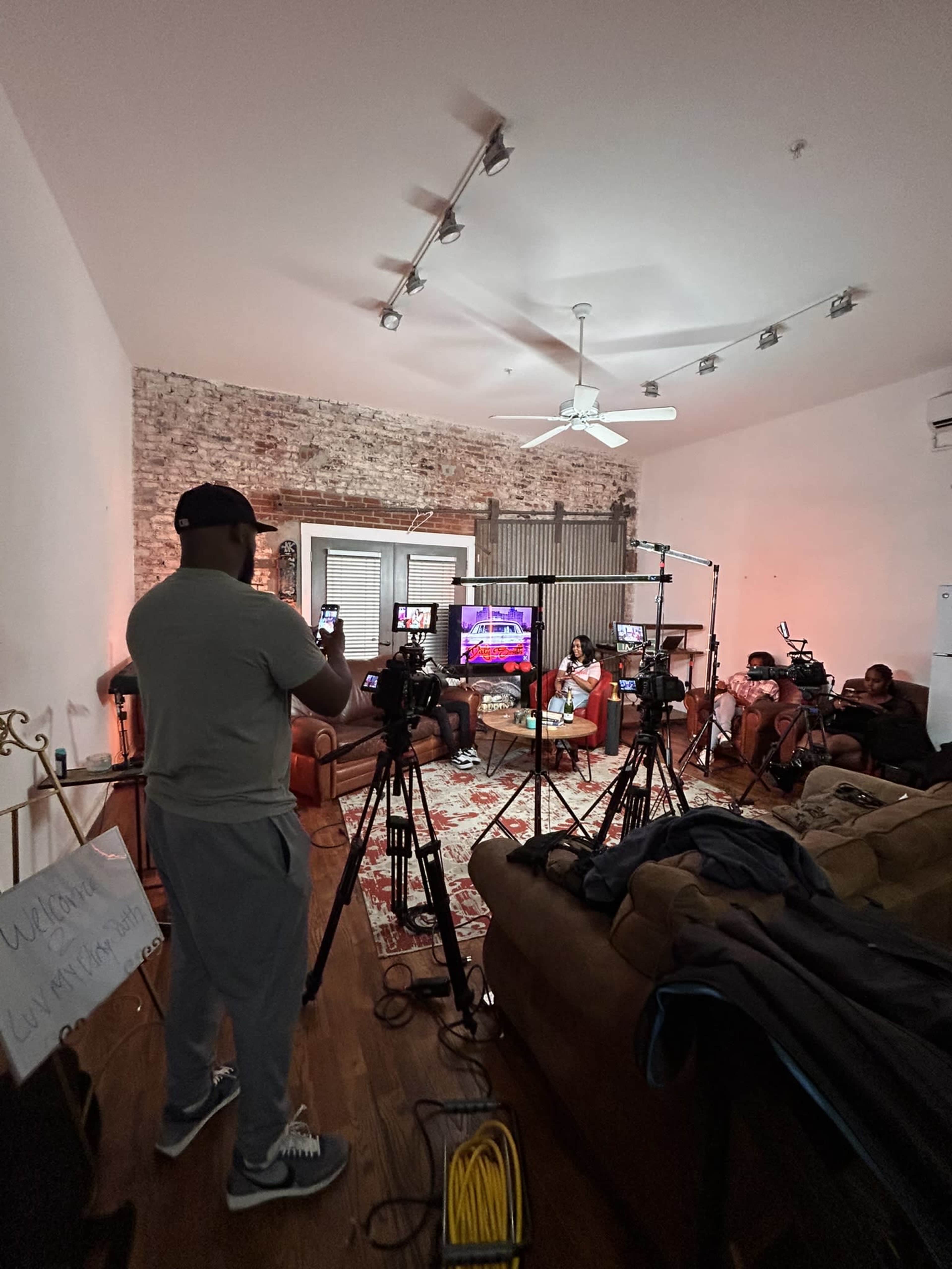 A person stands in a studio setting surrounded by multiple cameras, preparing for a video production featuring a group seated on a couch.