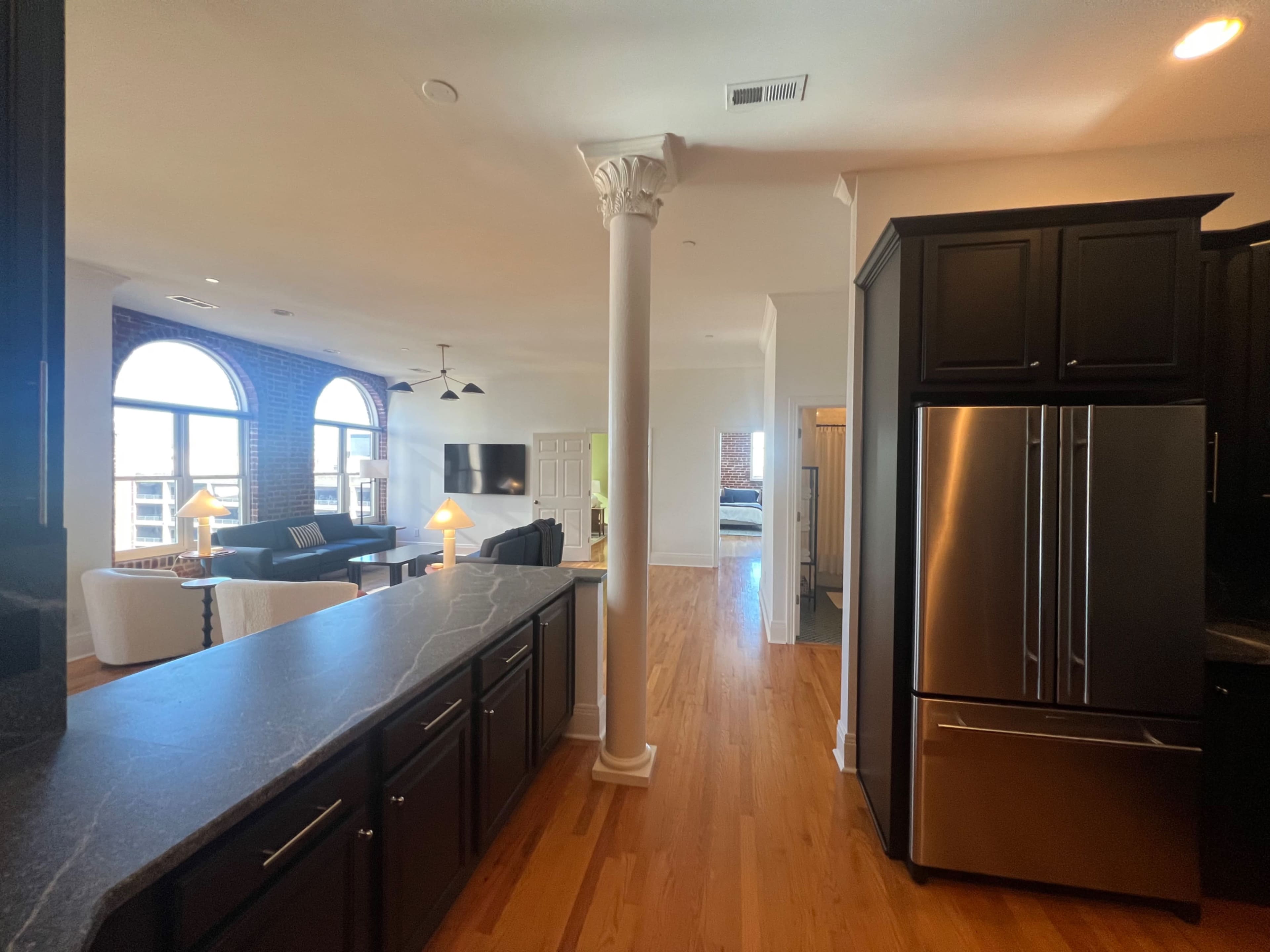 A spacious open-concept kitchen and living area featuring hardwood floors, a central column, and large windows that illuminate the space.