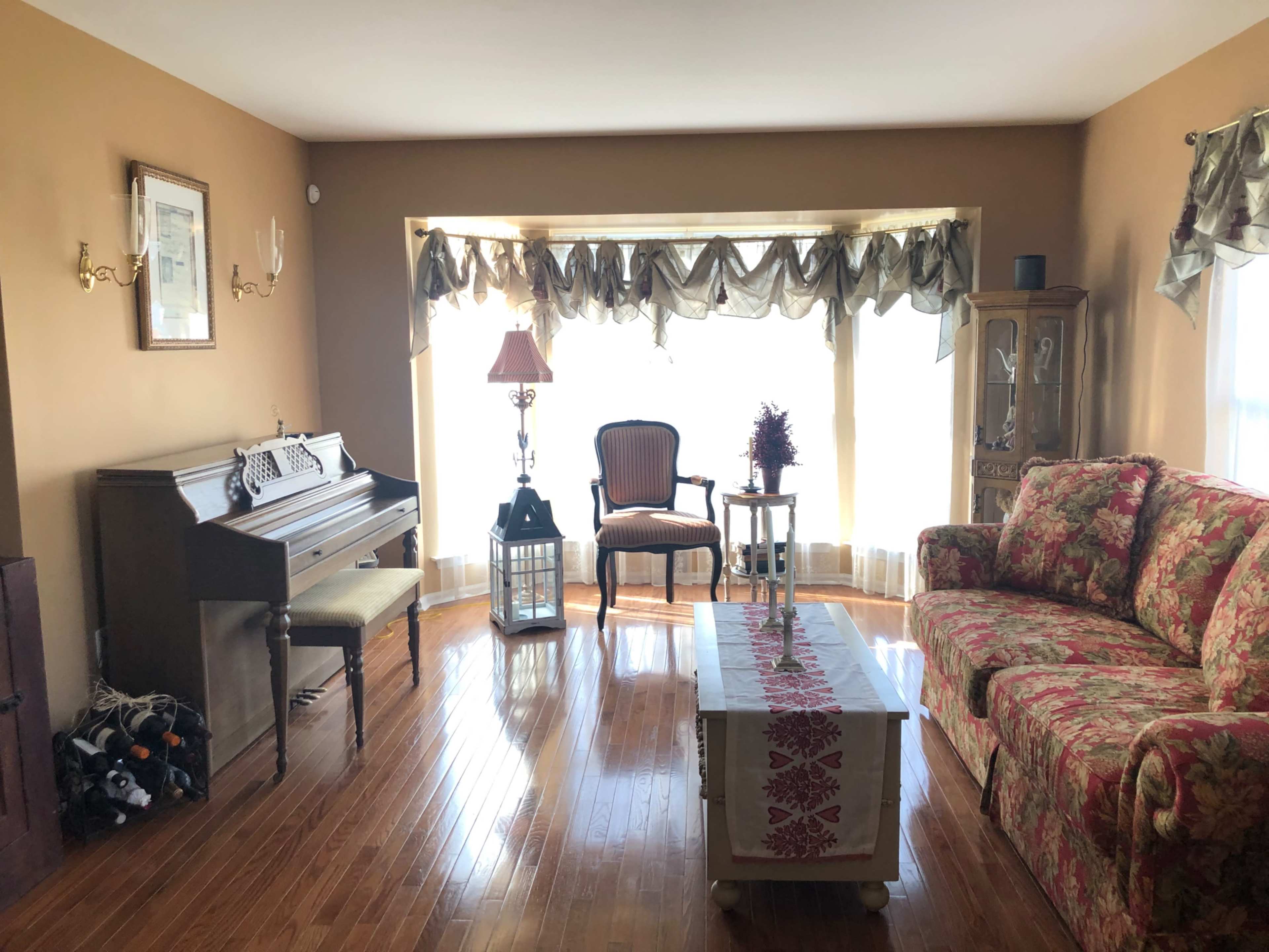The living room features a piano, a patterned sofa, and a large window with sheer curtains allowing natural light to fill the space.