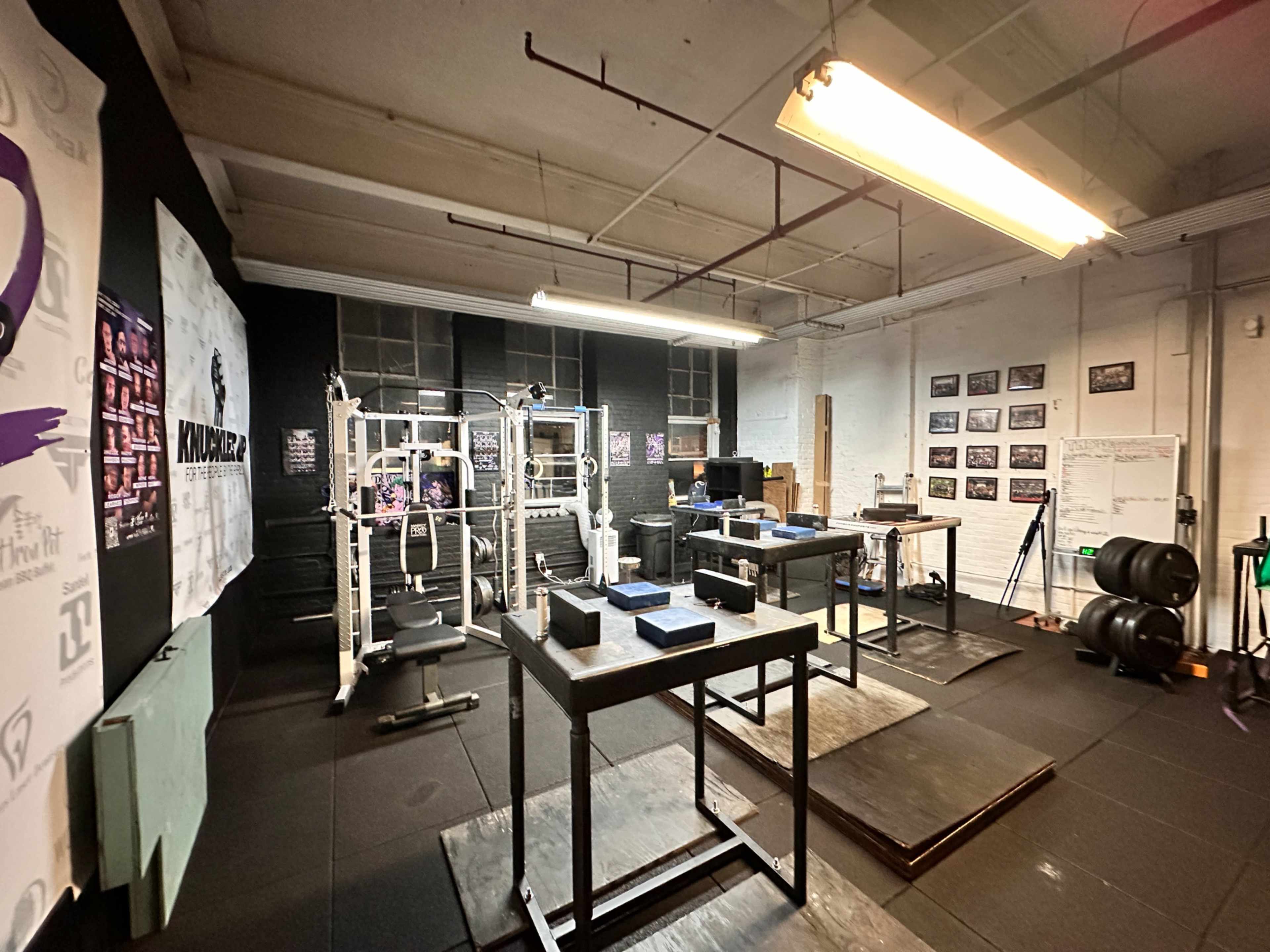 The image shows a gym interior equipped with weightlifting machines, benches, and various gym equipment arranged on black flooring and near black-painted walls.