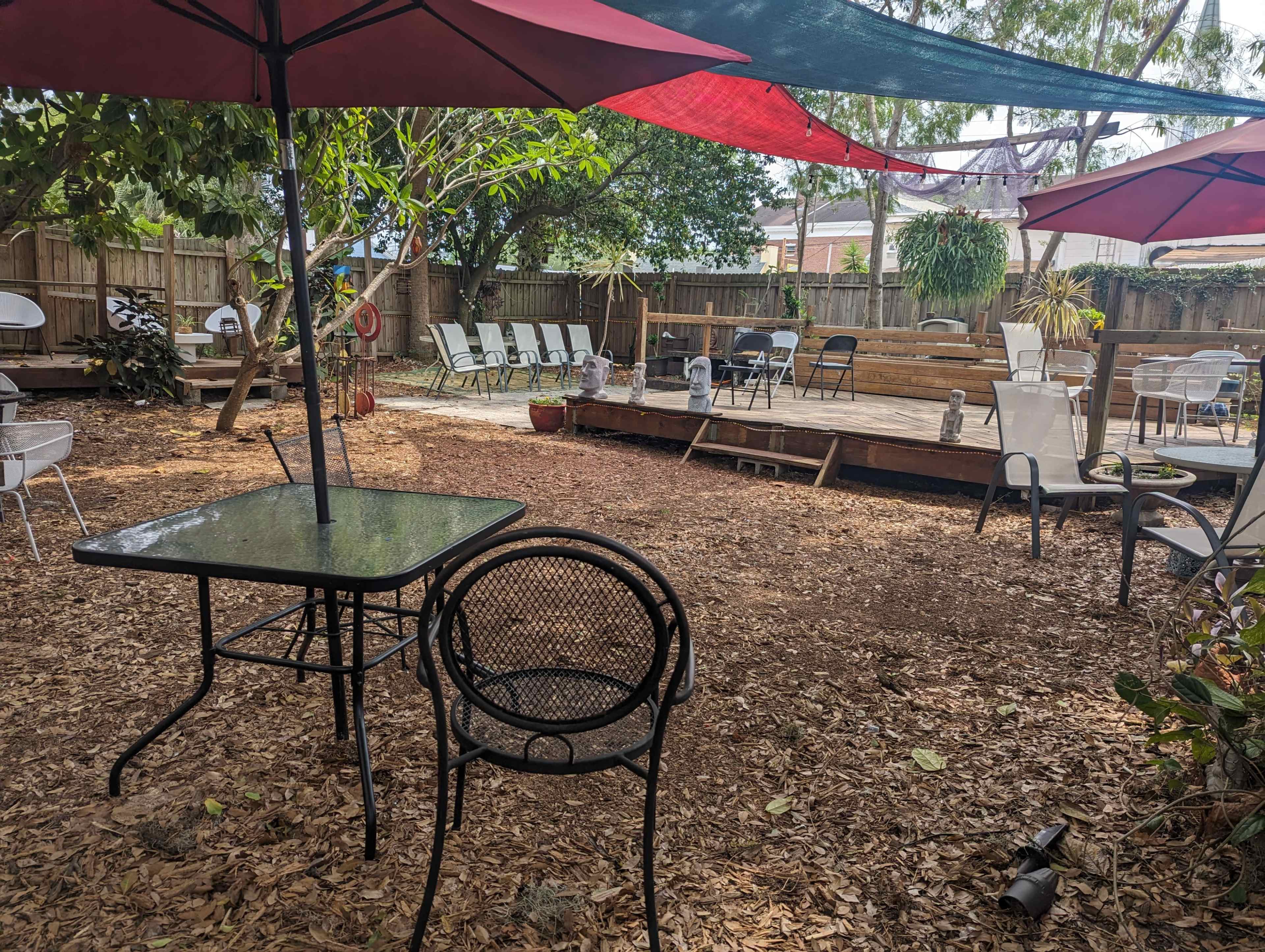 The image shows a backyard area featuring a wooden deck, scattered chairs, and several large umbrellas providing shade over a gravel and mulch ground.