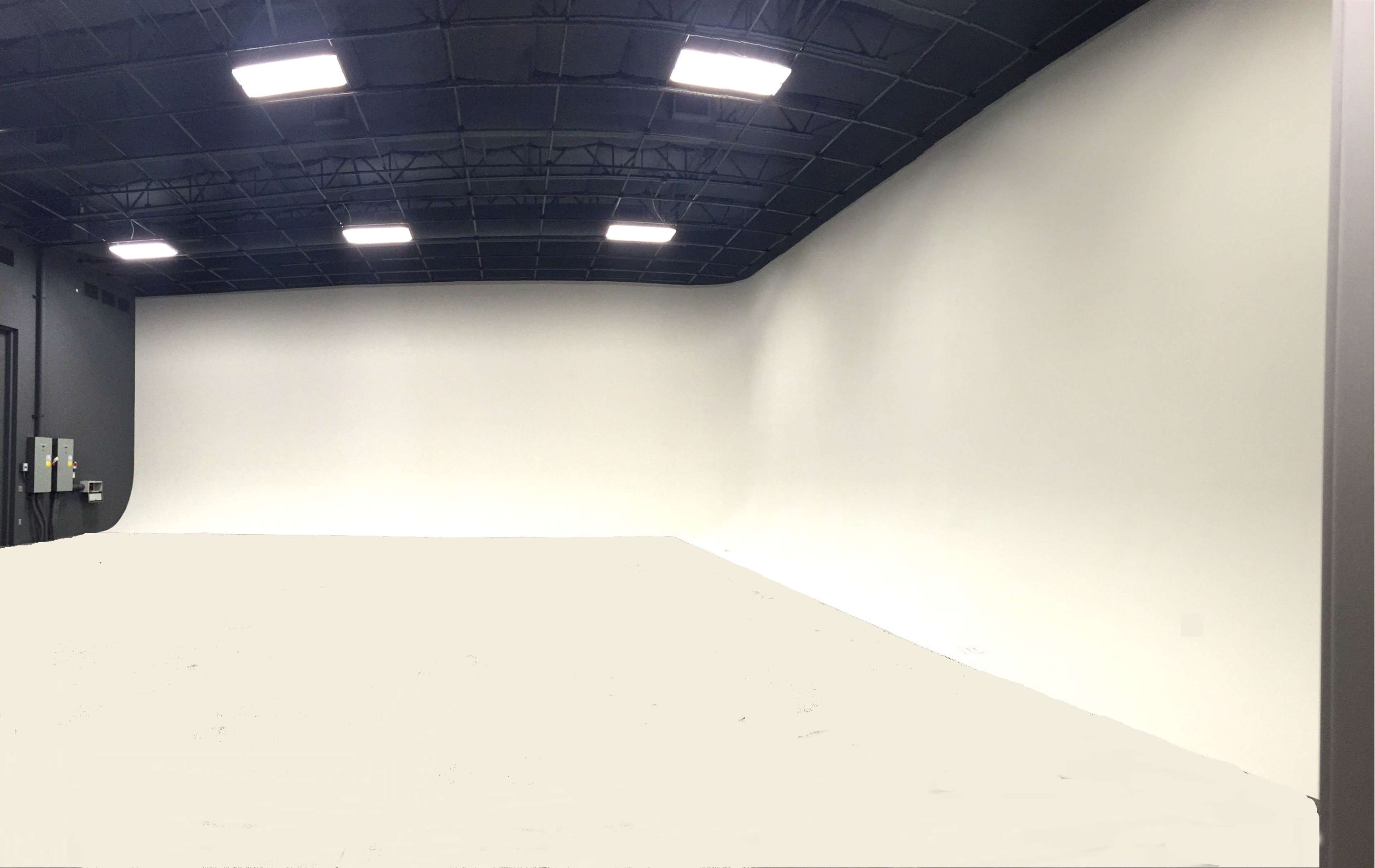 The image shows a large, empty studio space with a curved white backdrop and a black ceiling.