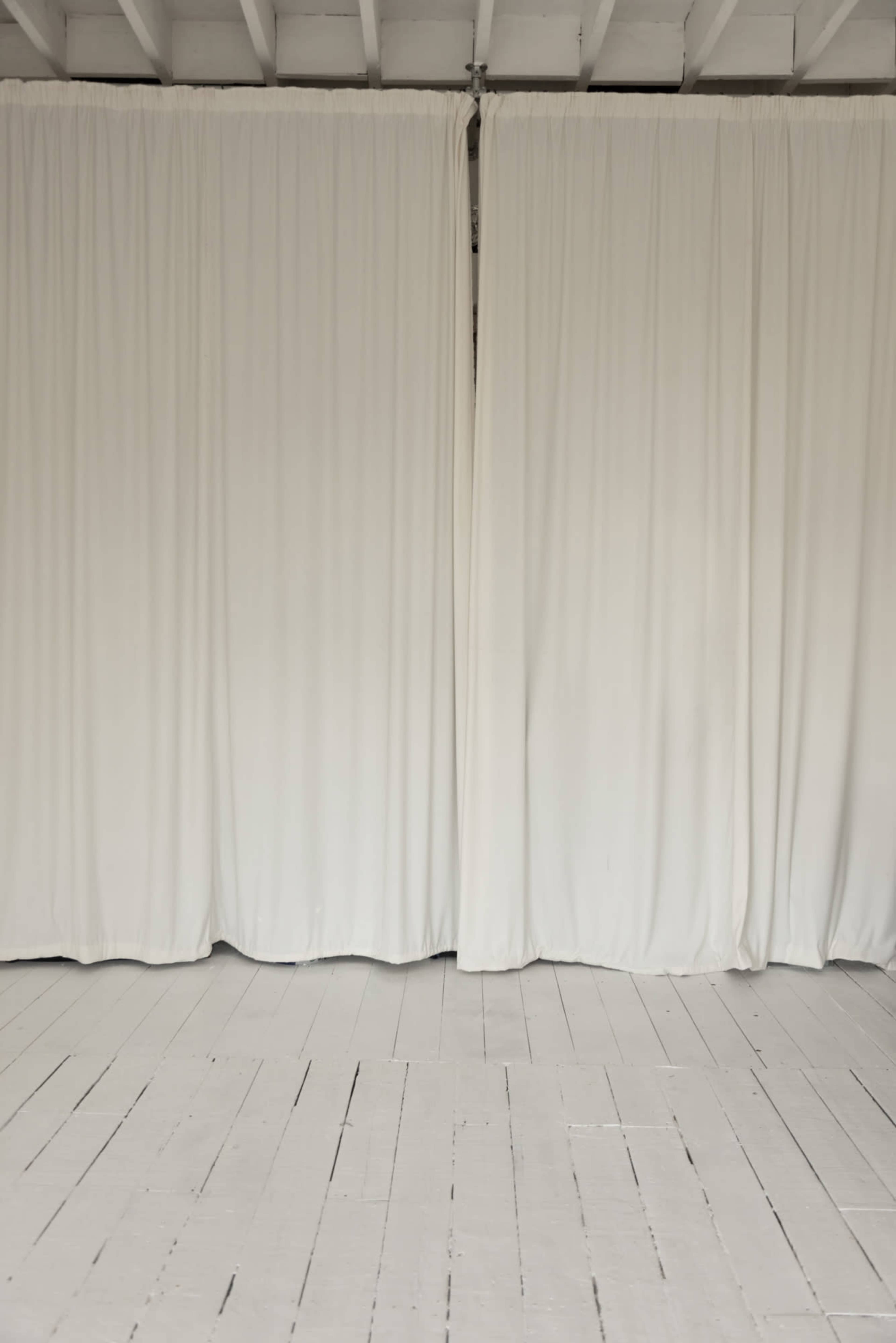The image shows a spacious interior with white curtains hanging from the ceiling and a light-colored wooden floor.
