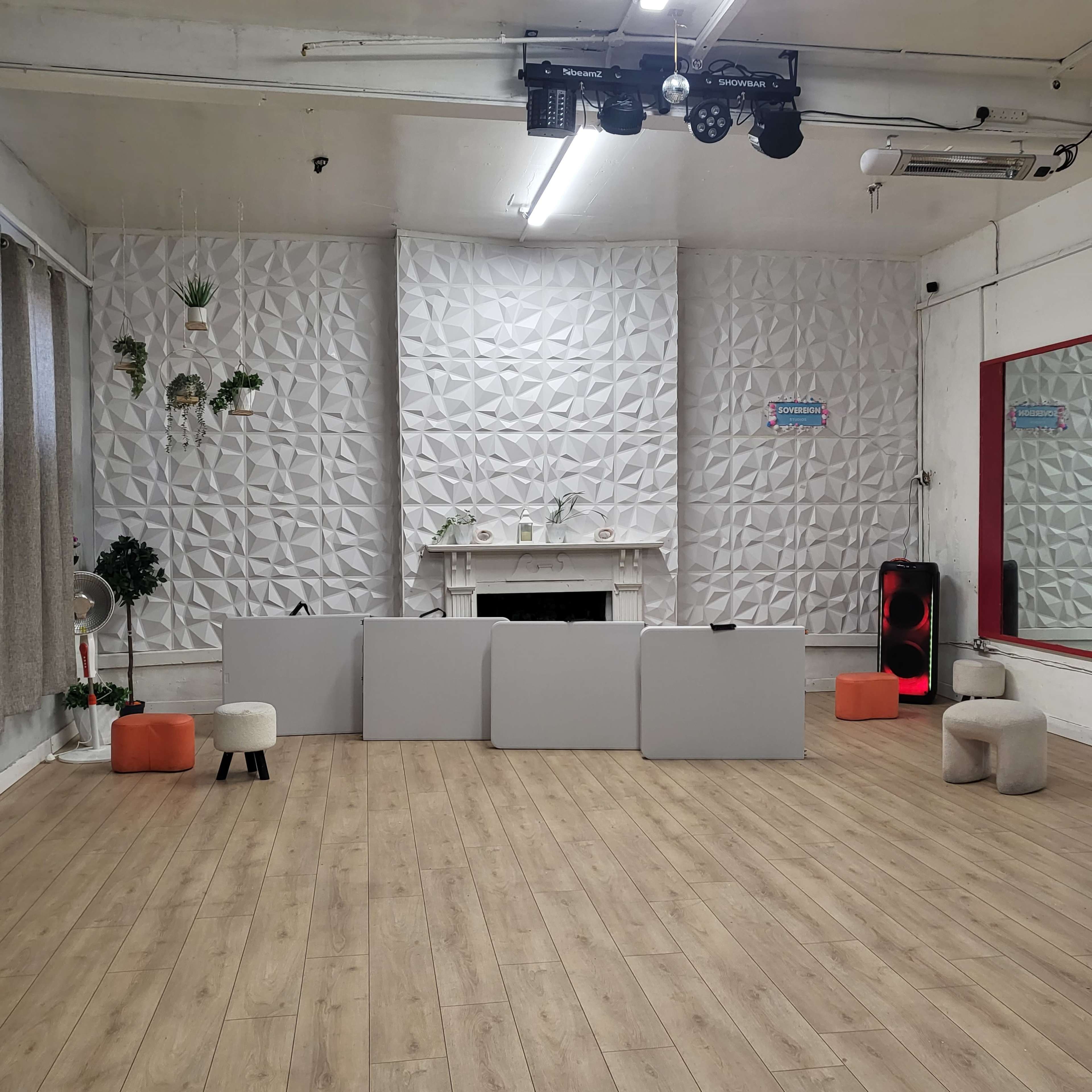 The image shows a spacious interior with a textured white wall, a fireplace, and several minimalist seating options arranged in a classroom-style layout.
