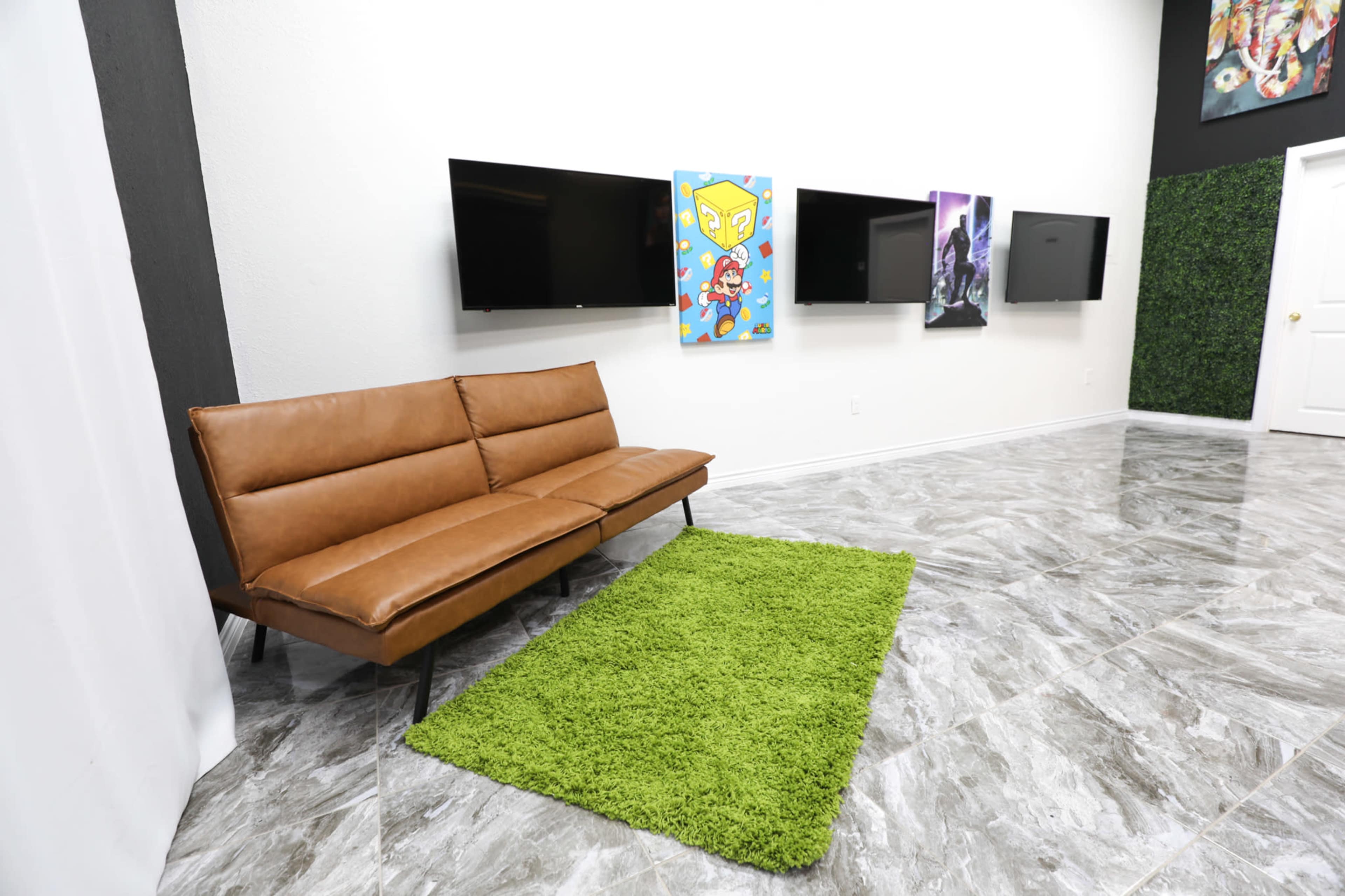 A modern interior space with a brown couch, a green rug, and multiple framed artworks displayed on the wall opposite two flat-screen televisions.