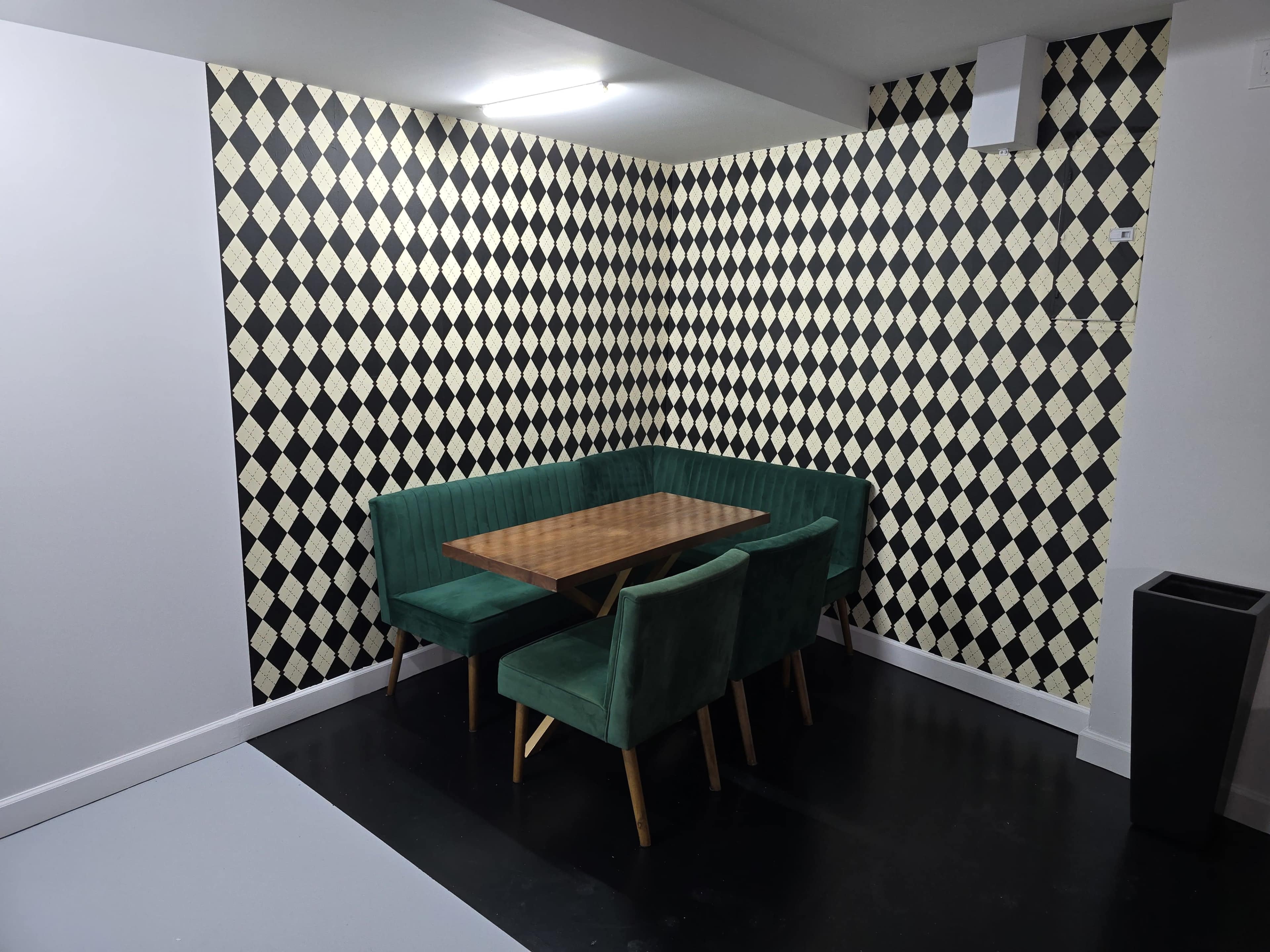 The image shows a corner dining area with a wooden table surrounded by green velvet benches and chairs, against a patterned black and white wall.