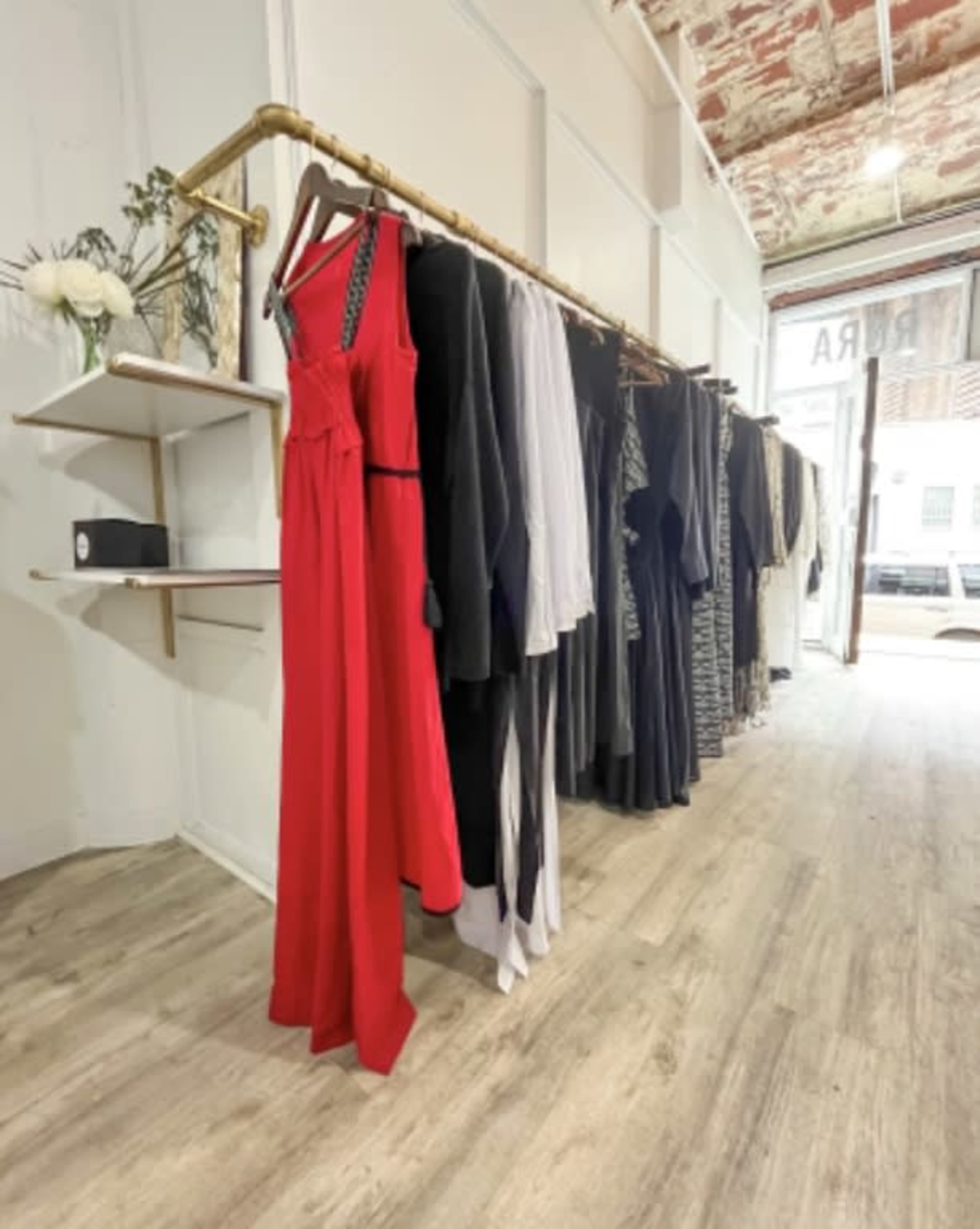 A clothing rack displays a variety of garments, including a red dress, in a boutique with a rustic interior.