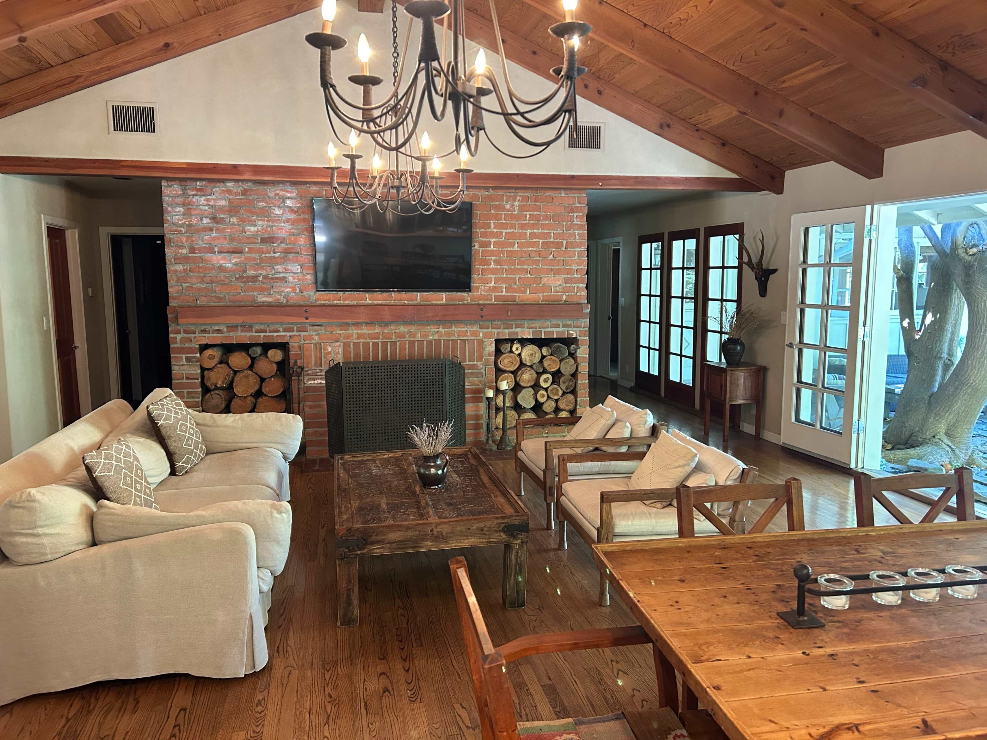 A cozy living room with a brick fireplace, wooden ceiling beams, and a mix of comfortable seating arrangements.