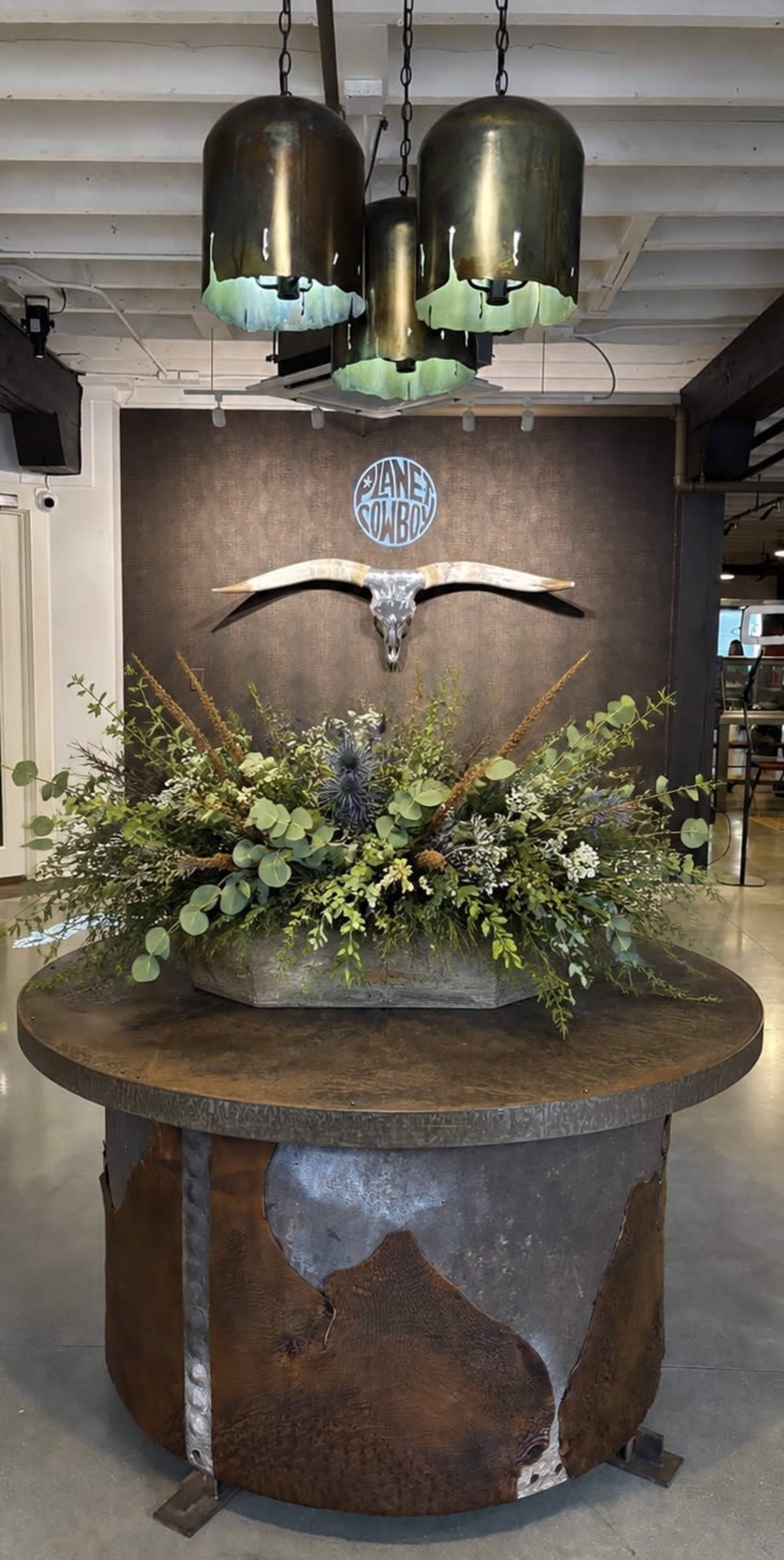 The image shows a circular table adorned with a floral arrangement, topped by a decorative skull, beneath three pendant lights.