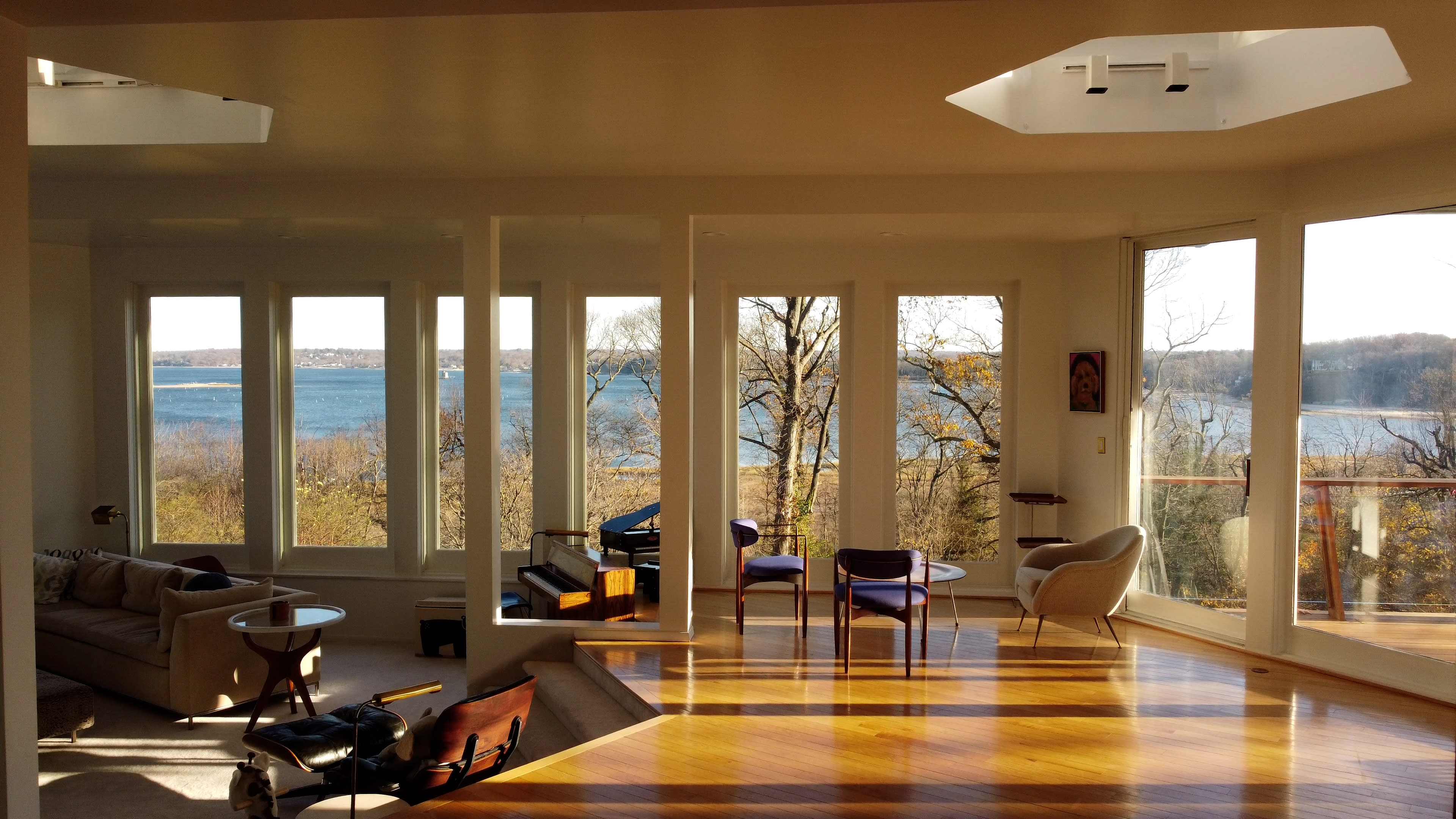 A spacious living area with large windows overlooking a body of water and trees in the distance.
