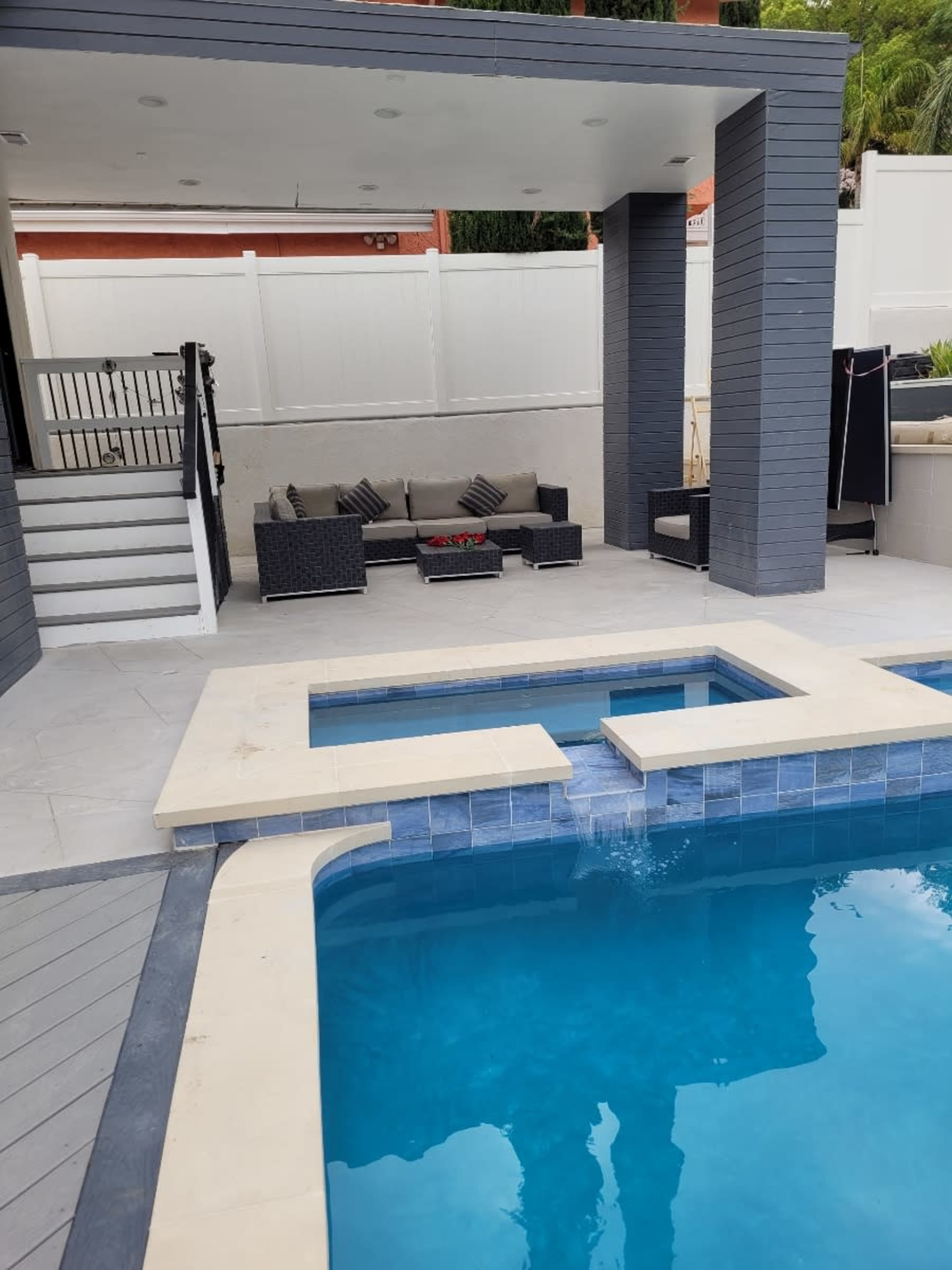 A modern pool area with a large swimming pool, a spa section, and a shaded seating area with outdoor furniture nearby.