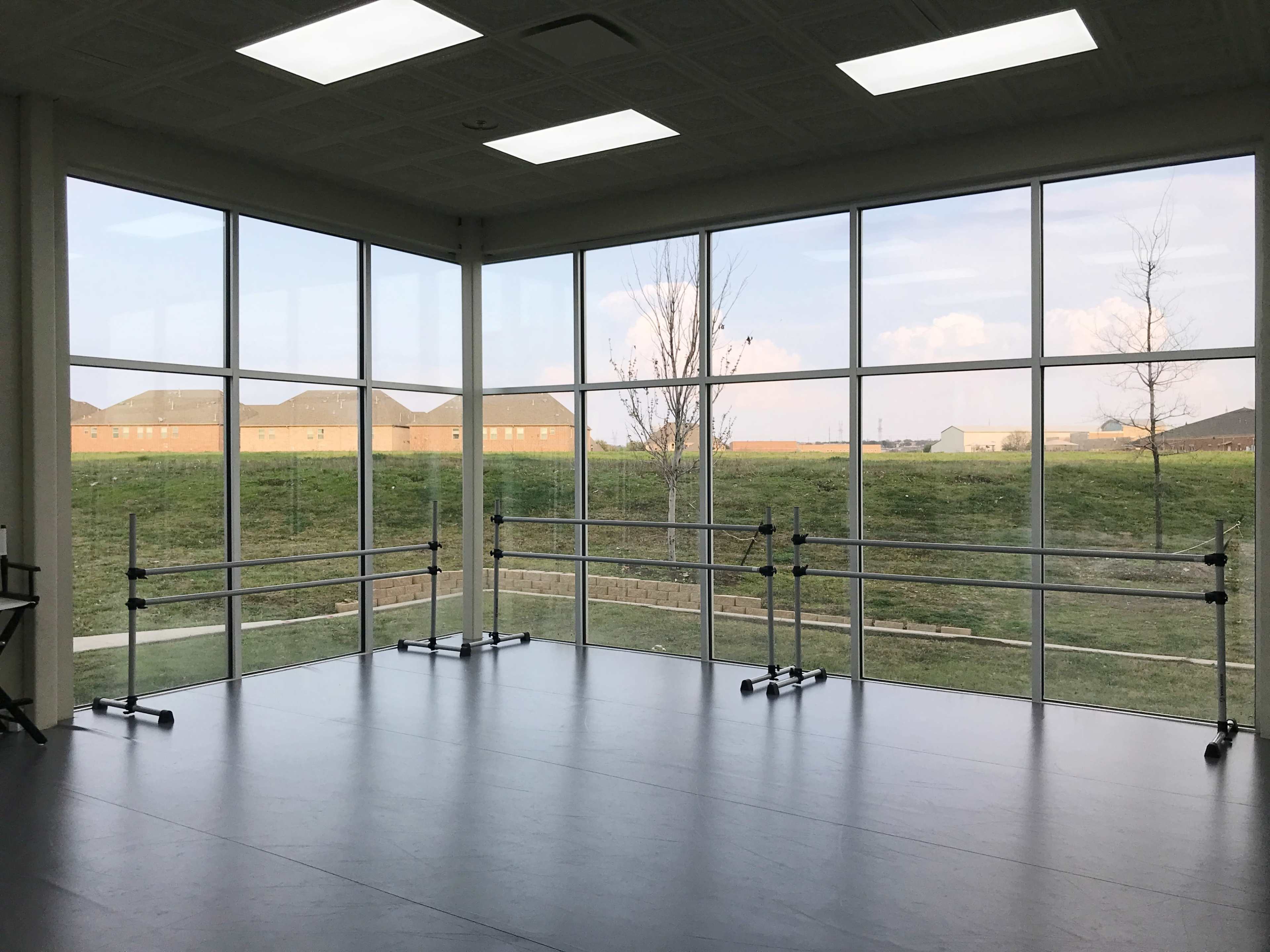 A dance studio features large windows overlooking an open grassy area and distant buildings.