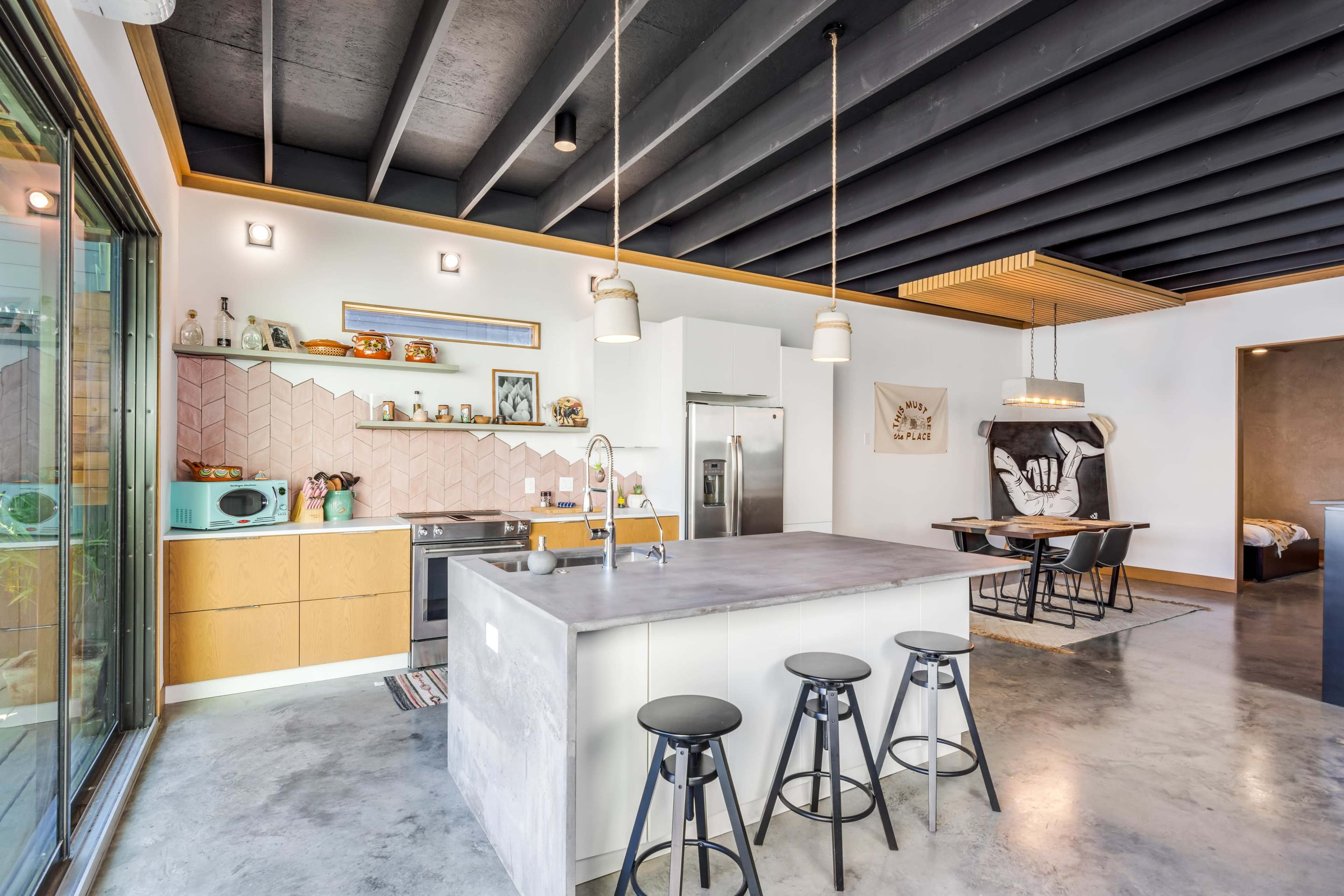 A modern kitchen featuring a central island with bar stools, stainless steel appliances, and a dining area with a table.