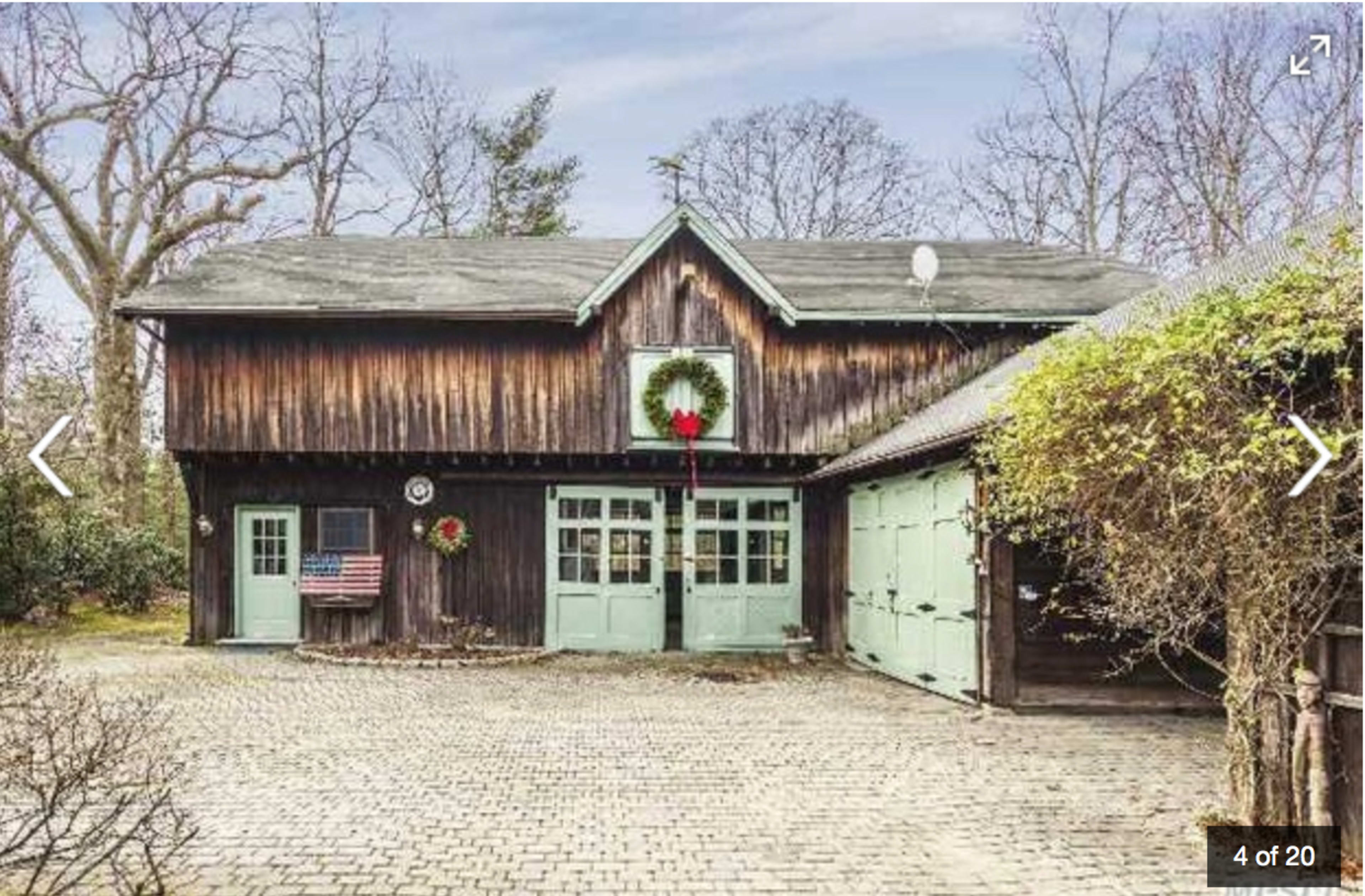The image shows a two-story wooden building with a wreath on the front door and an American flag hanging to the left.