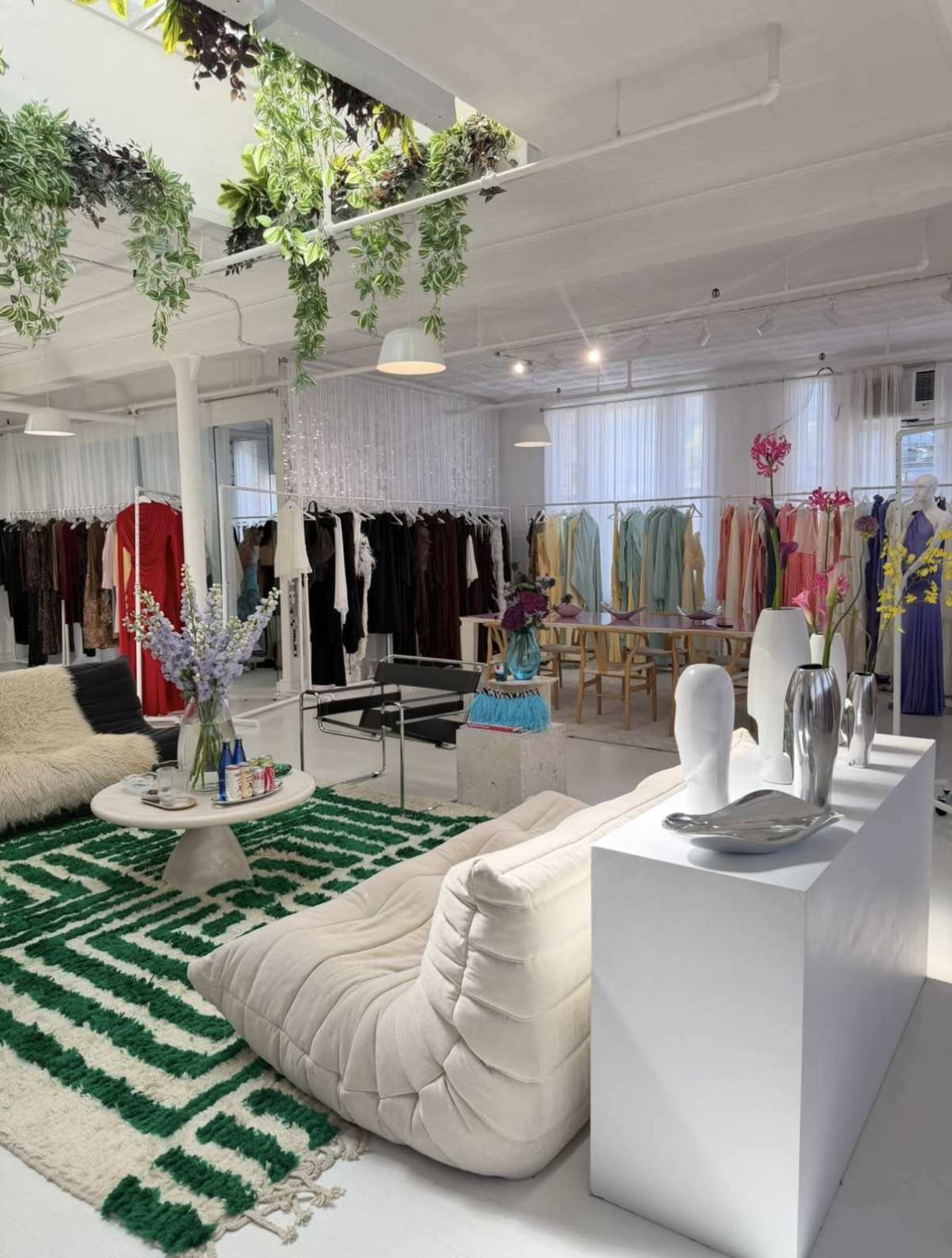 The image shows a modern retail space featuring a stylish seating area with a green and white rug, surrounded by clothing racks displaying various garments.