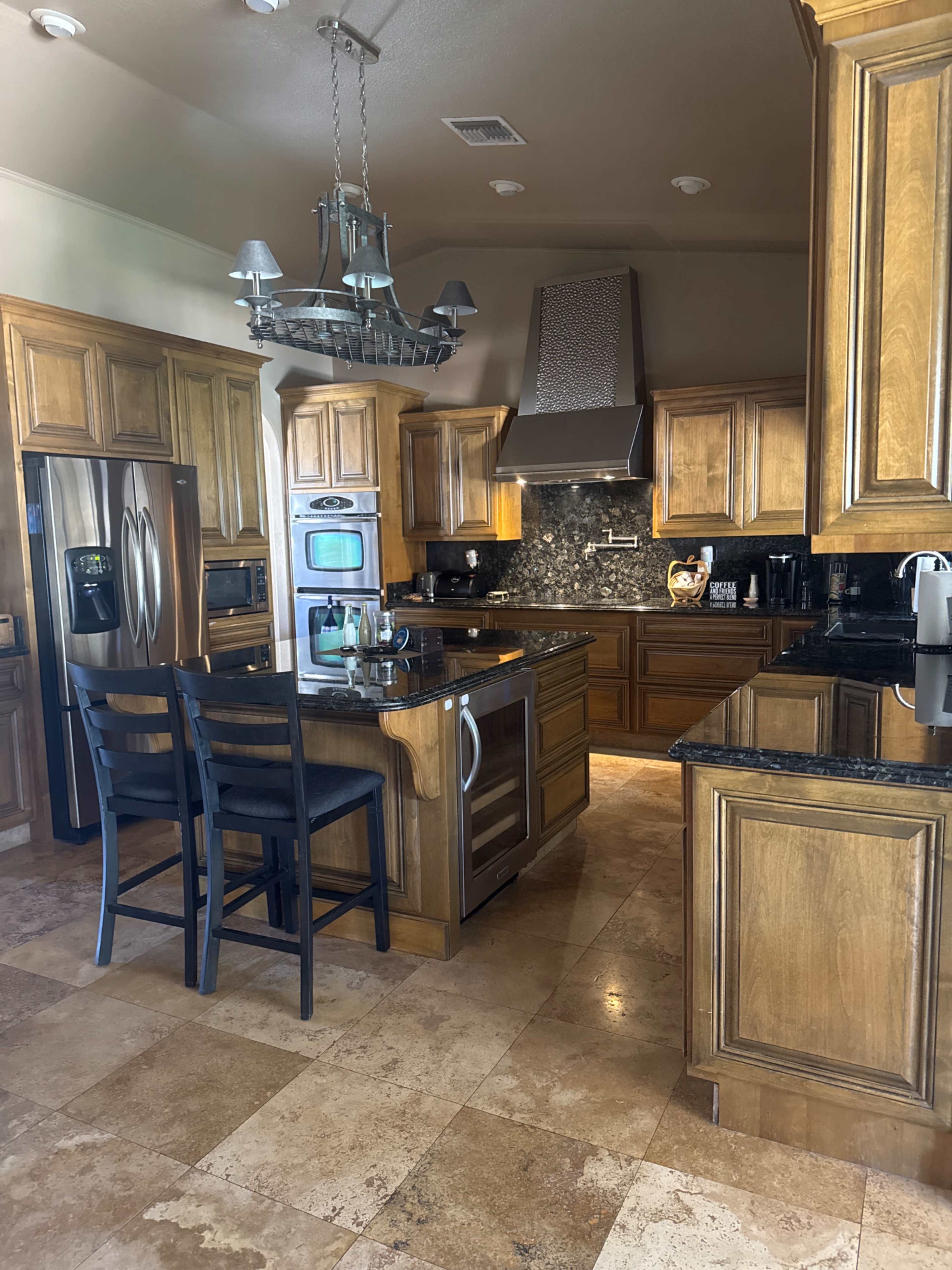 The image shows a spacious kitchen with wooden cabinetry, a large island, and modern appliances, featuring a tile floor.