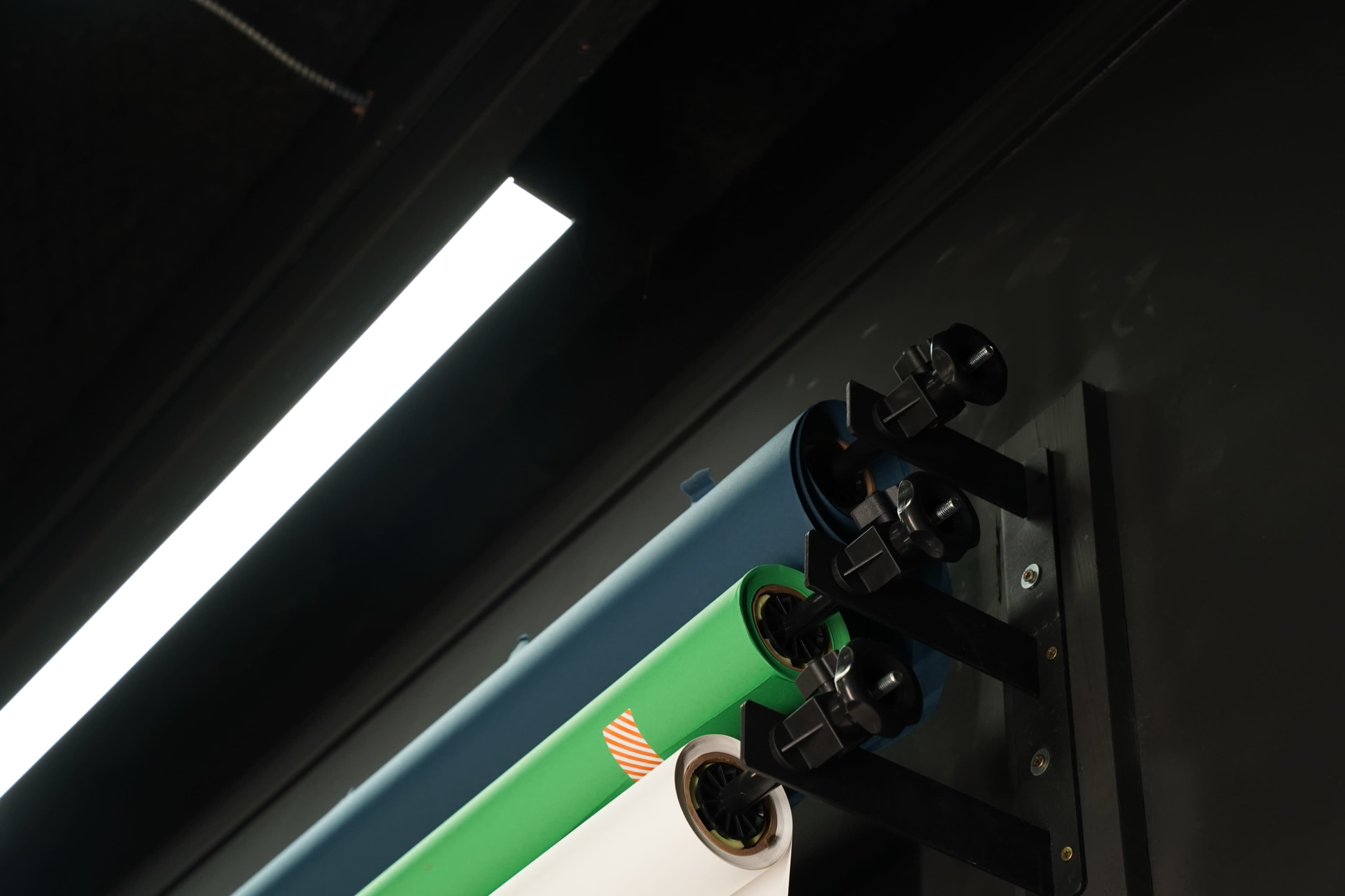 A close-up of a wall-mounted rack holding three rolls of colored paper secured with black clamps.