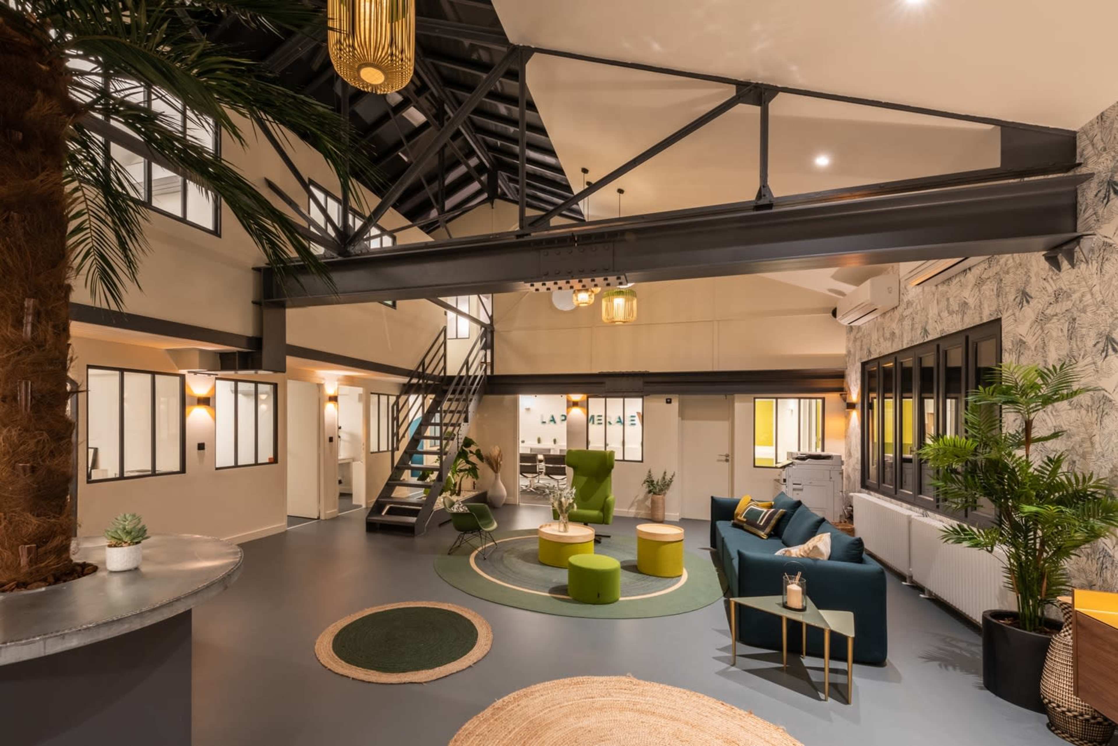 The image depicts a modern, open-concept lounge area featuring a mix of green and neutral furnishings, large windows, and a spiral staircase leading to an upper level.
