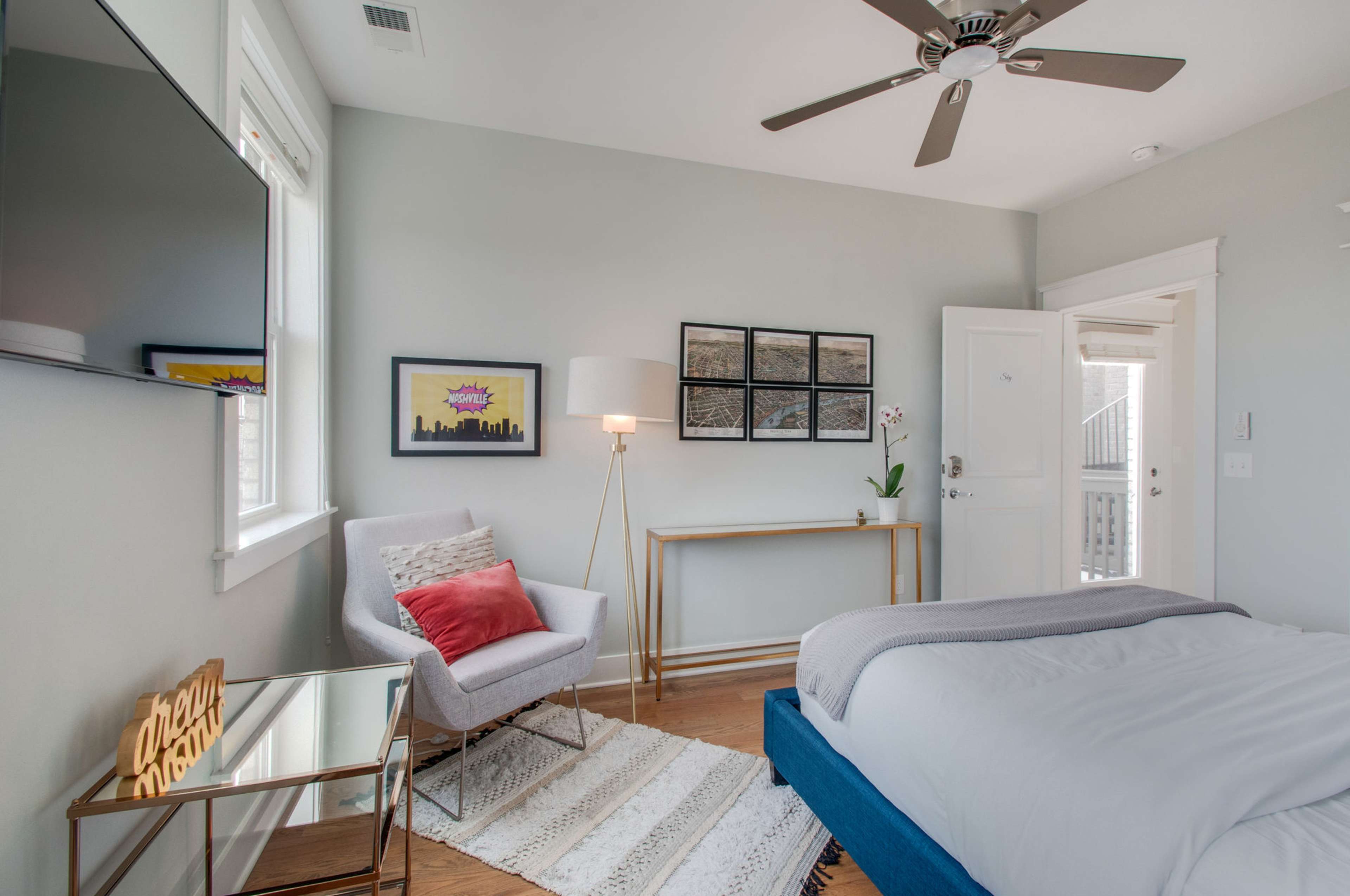 The image shows a well-lit bedroom featuring a bed, a chair, a coffee table, and wall art.