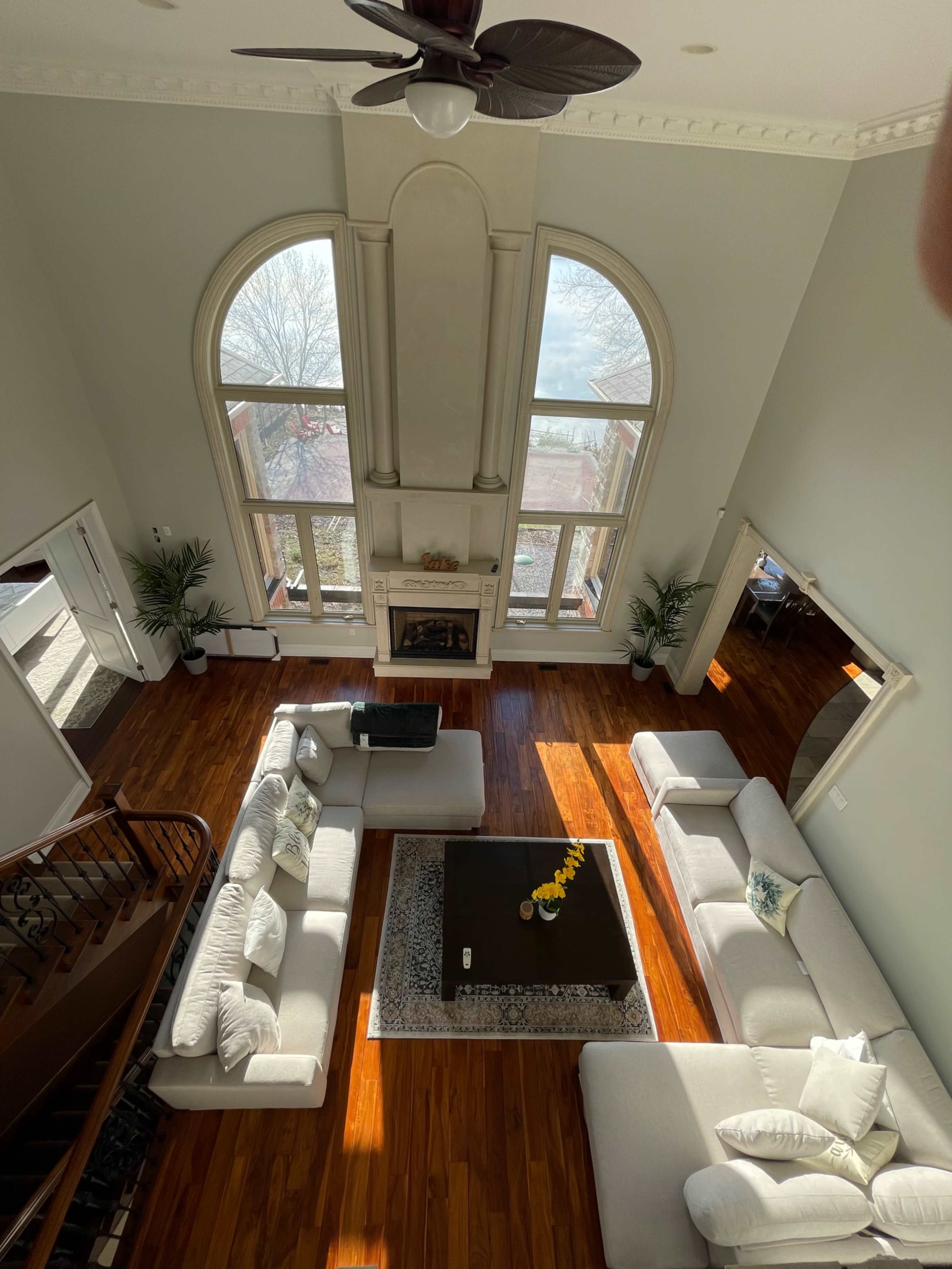 A spacious living room with large windows, a central coffee table, and beige sofas arranged around a wooden floor.