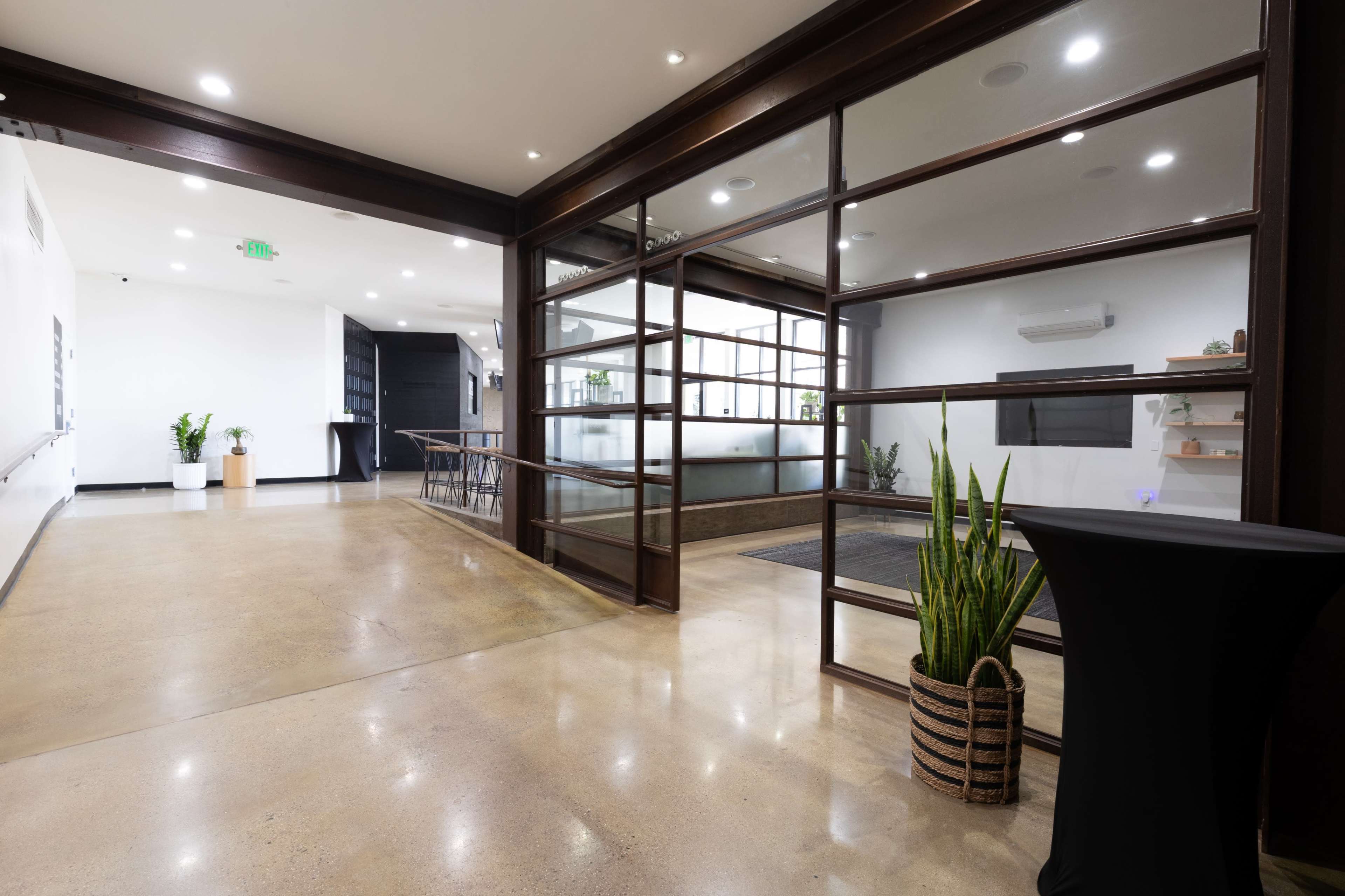 The image shows a modern interior space featuring a glass and wood partition, polished concrete floors, and indoor plants.