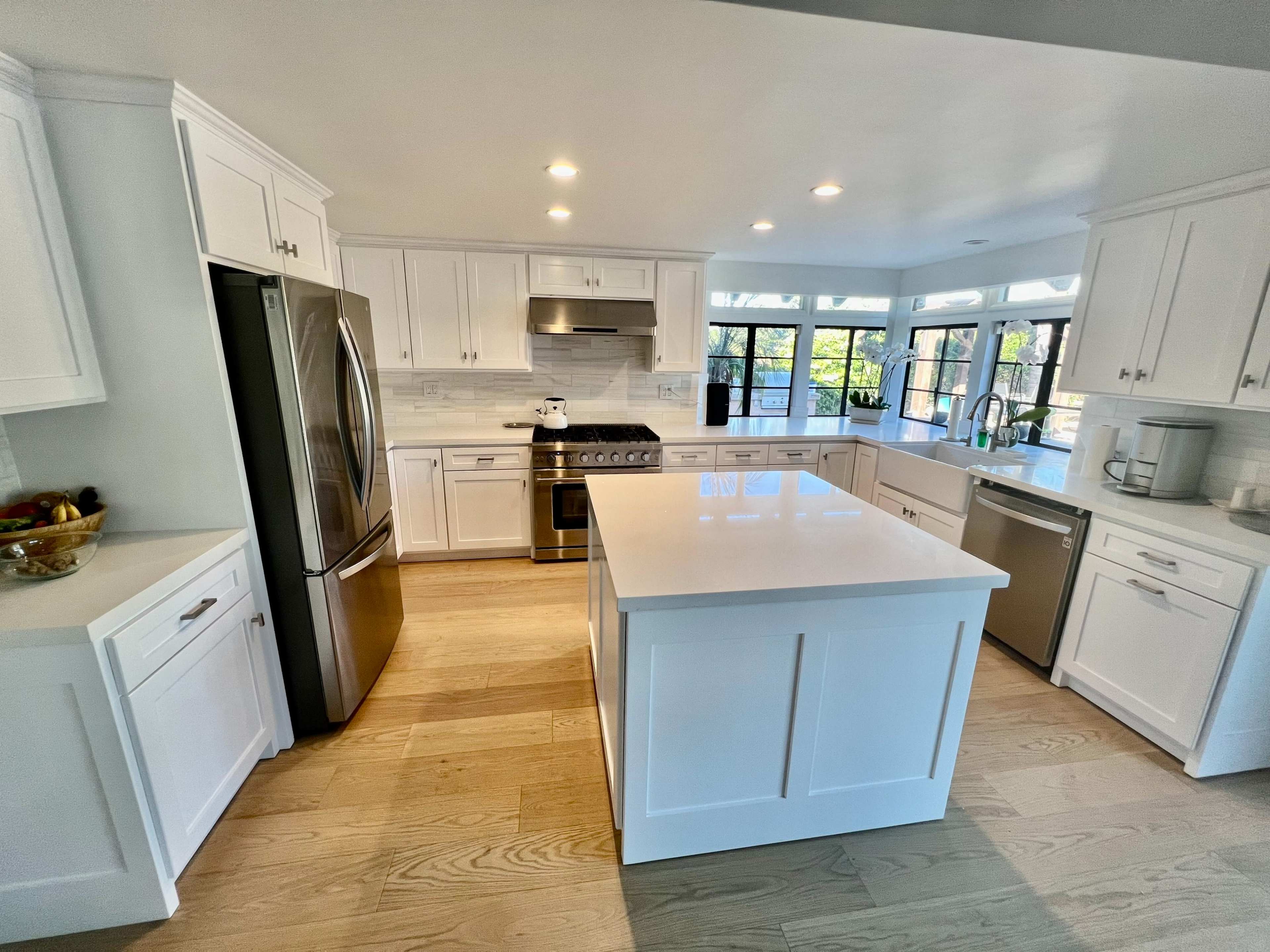 A modern kitchen features white cabinetry, stainless steel appliances, and a large central island with a light countertop.