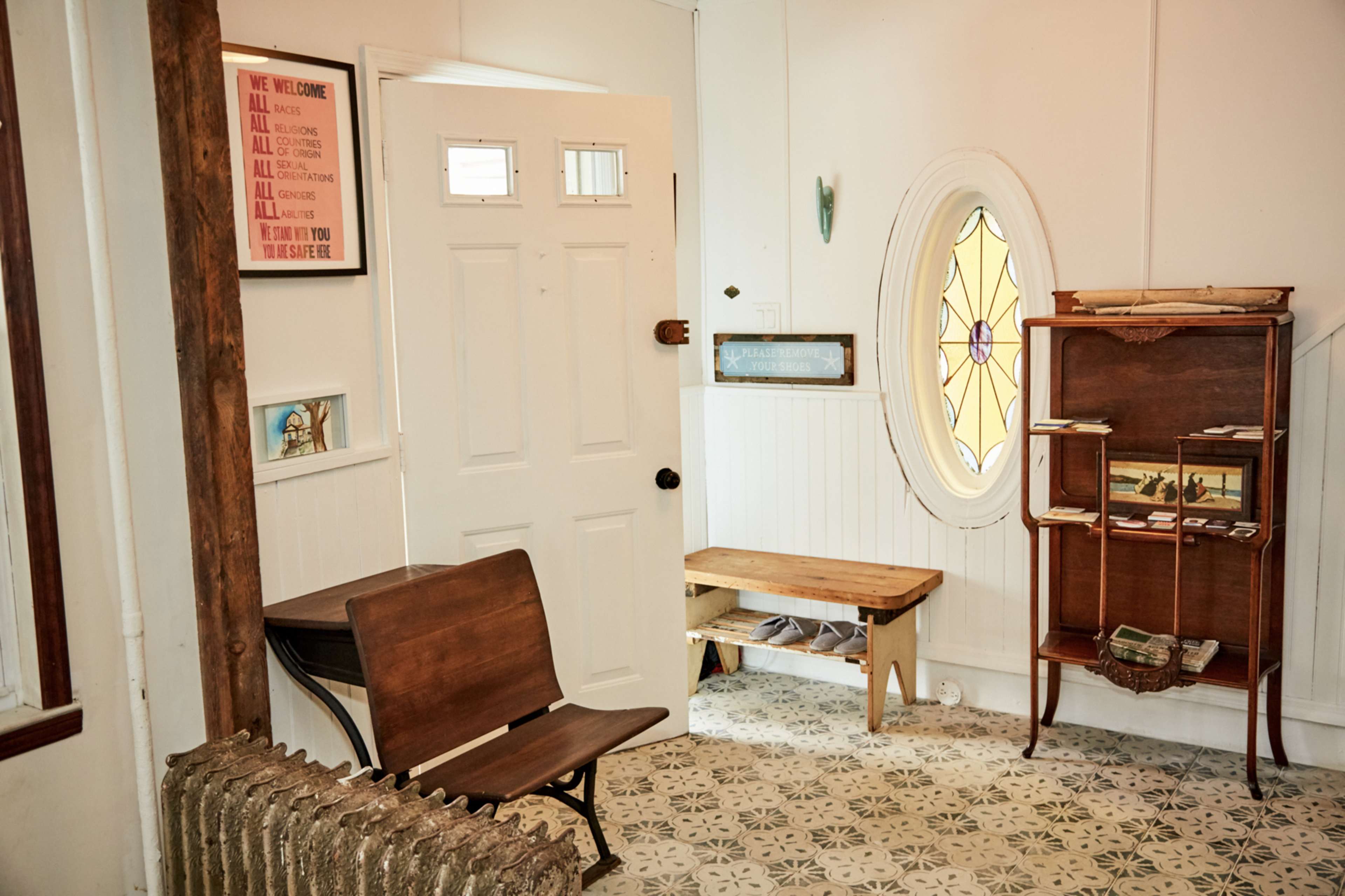 The entryway features a wooden bench, a decorative radiator, a stained glass window, and a small bookshelf against the wall.