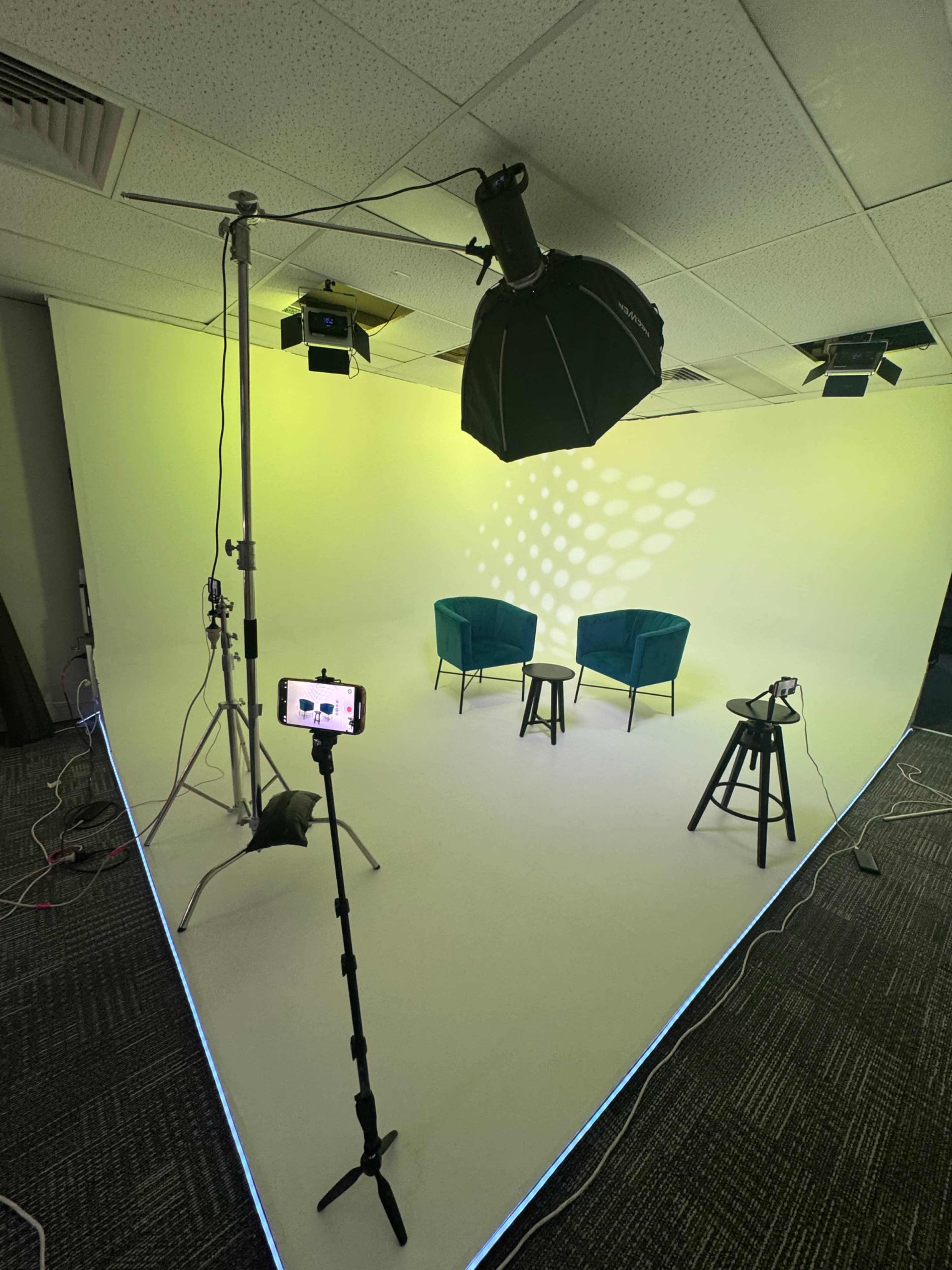 The image shows a minimalist studio setup with two teal chairs, a small table, and lighting equipment against a gradient backdrop.