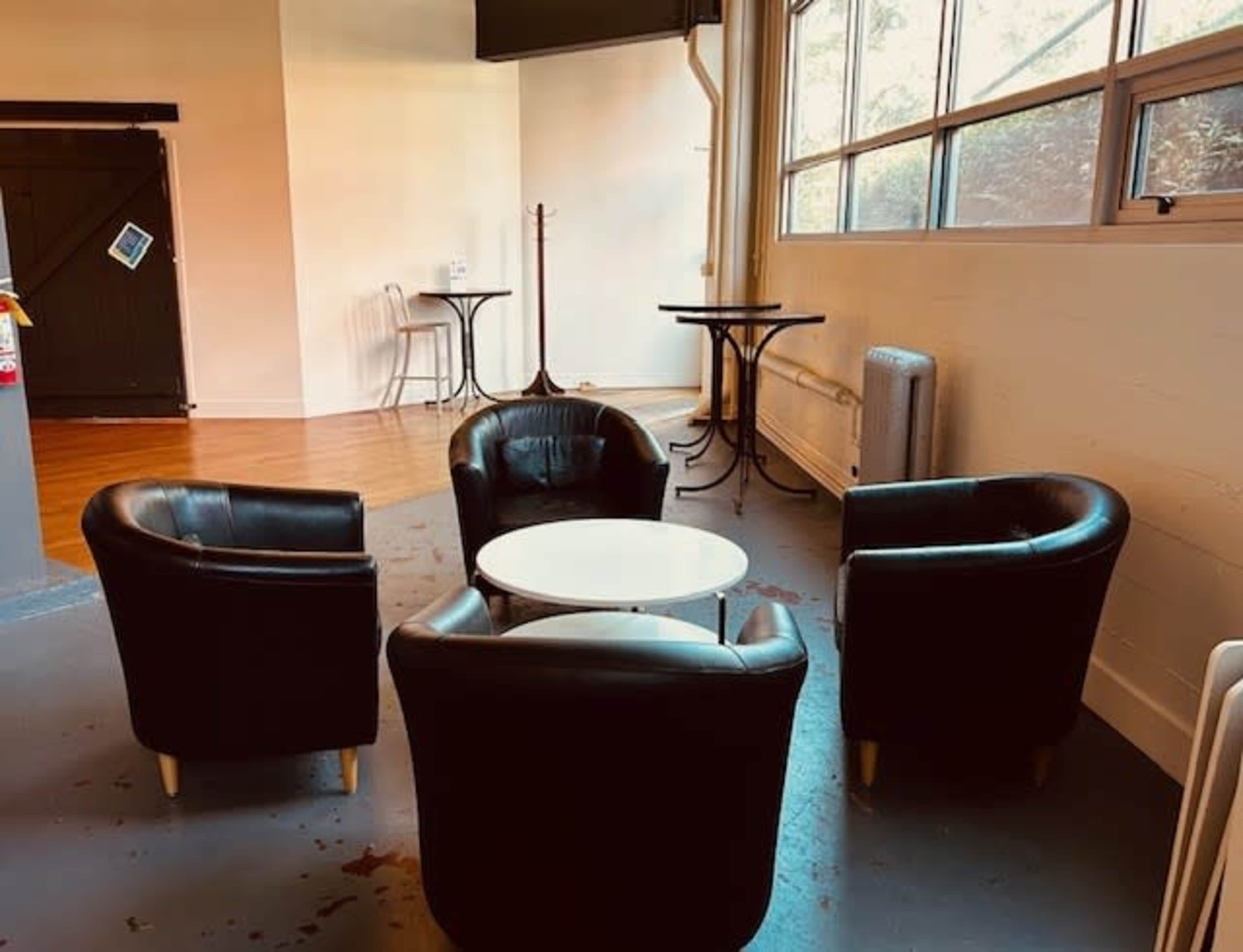 A small seating area with four black chairs arranged around a white table in a well-lit space with large windows.