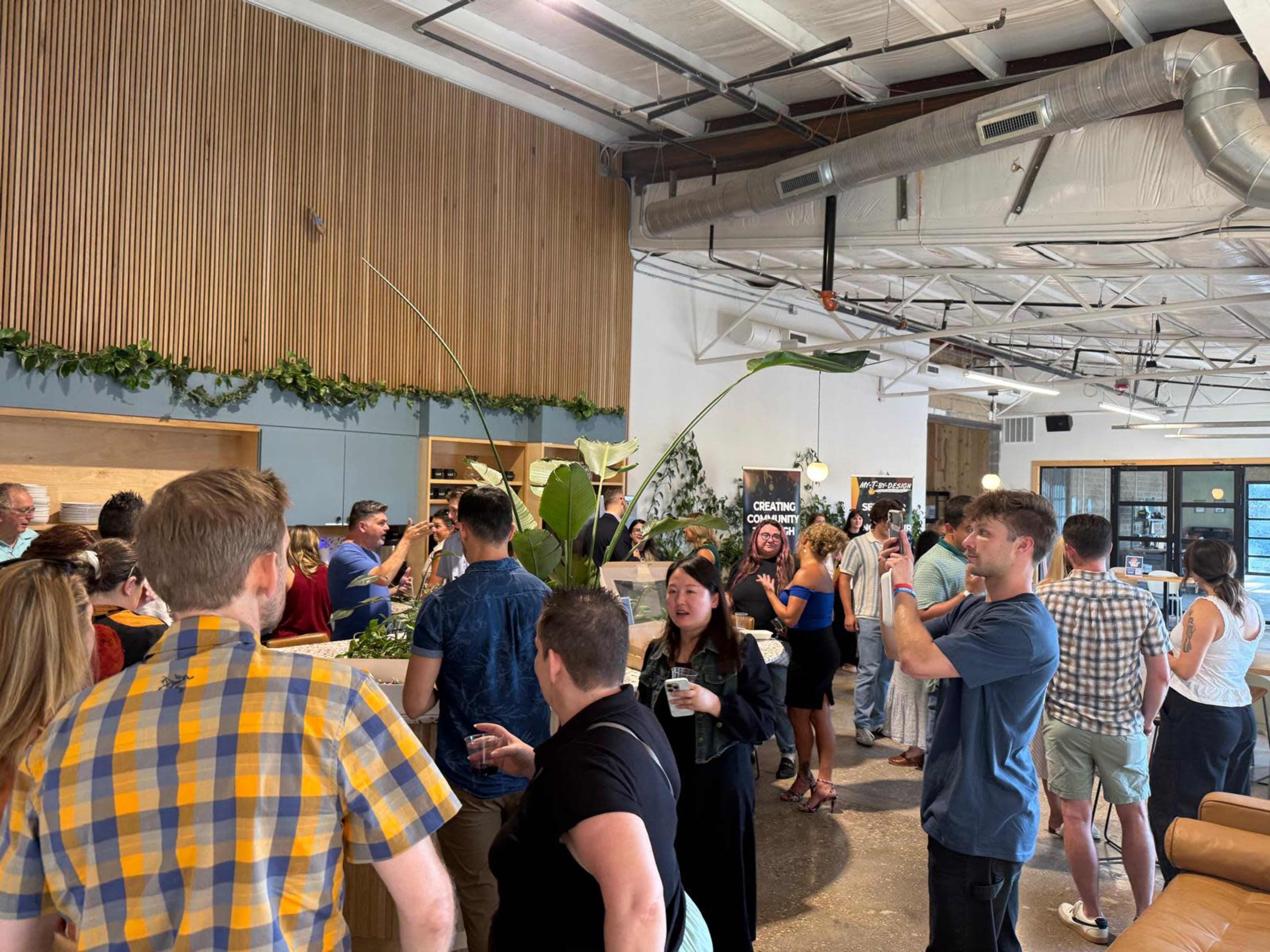 A crowd of people is gathered indoors around a reception area decorated with plants and wooden features.